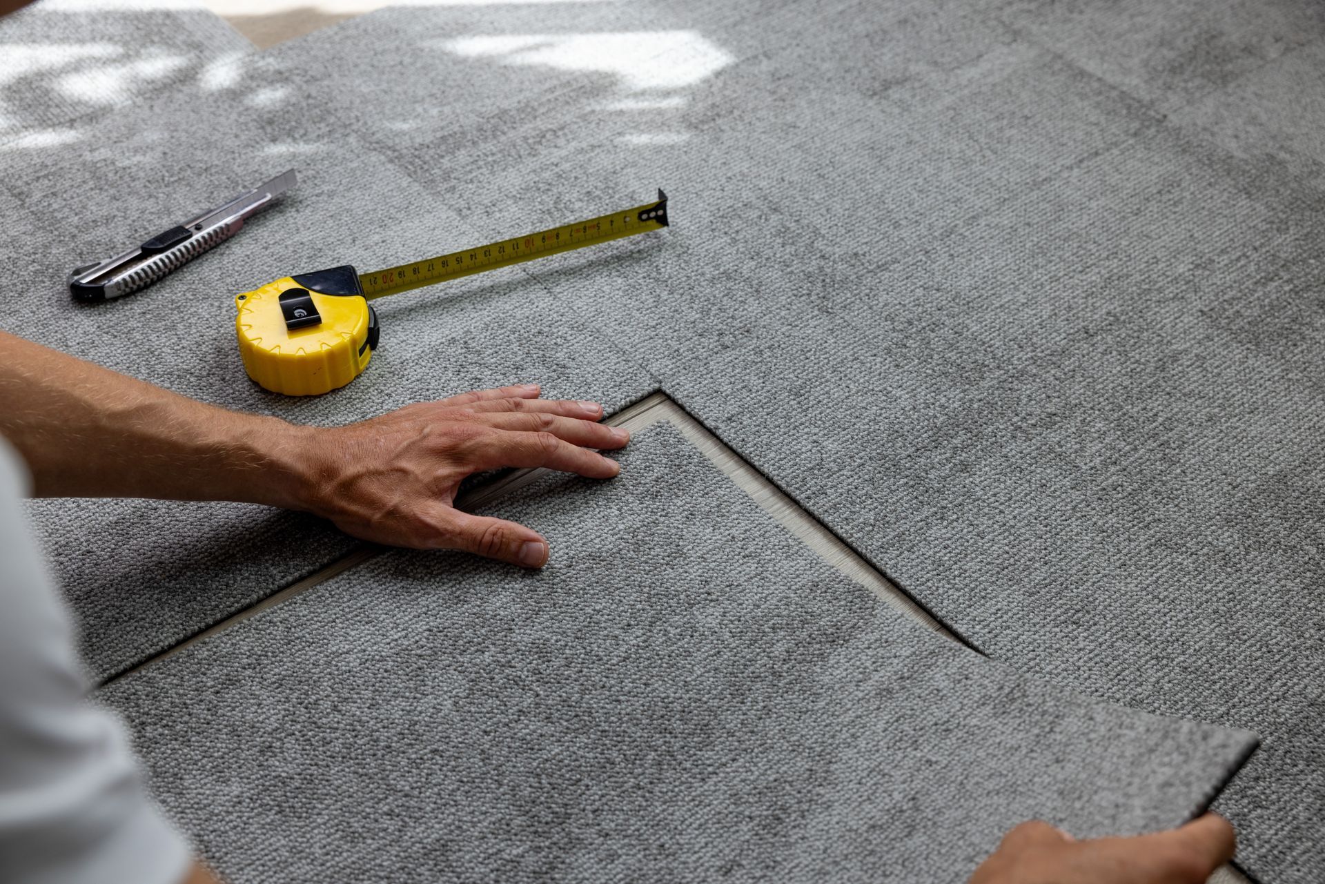 A man is measuring a piece of carpet with a tape measure.