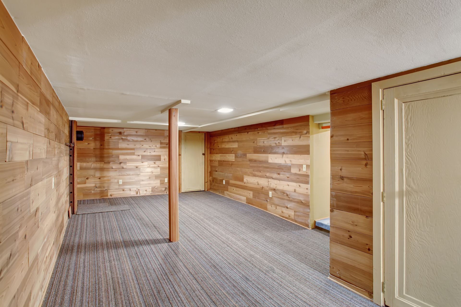 An empty basement with wooden walls and a carpeted floor.