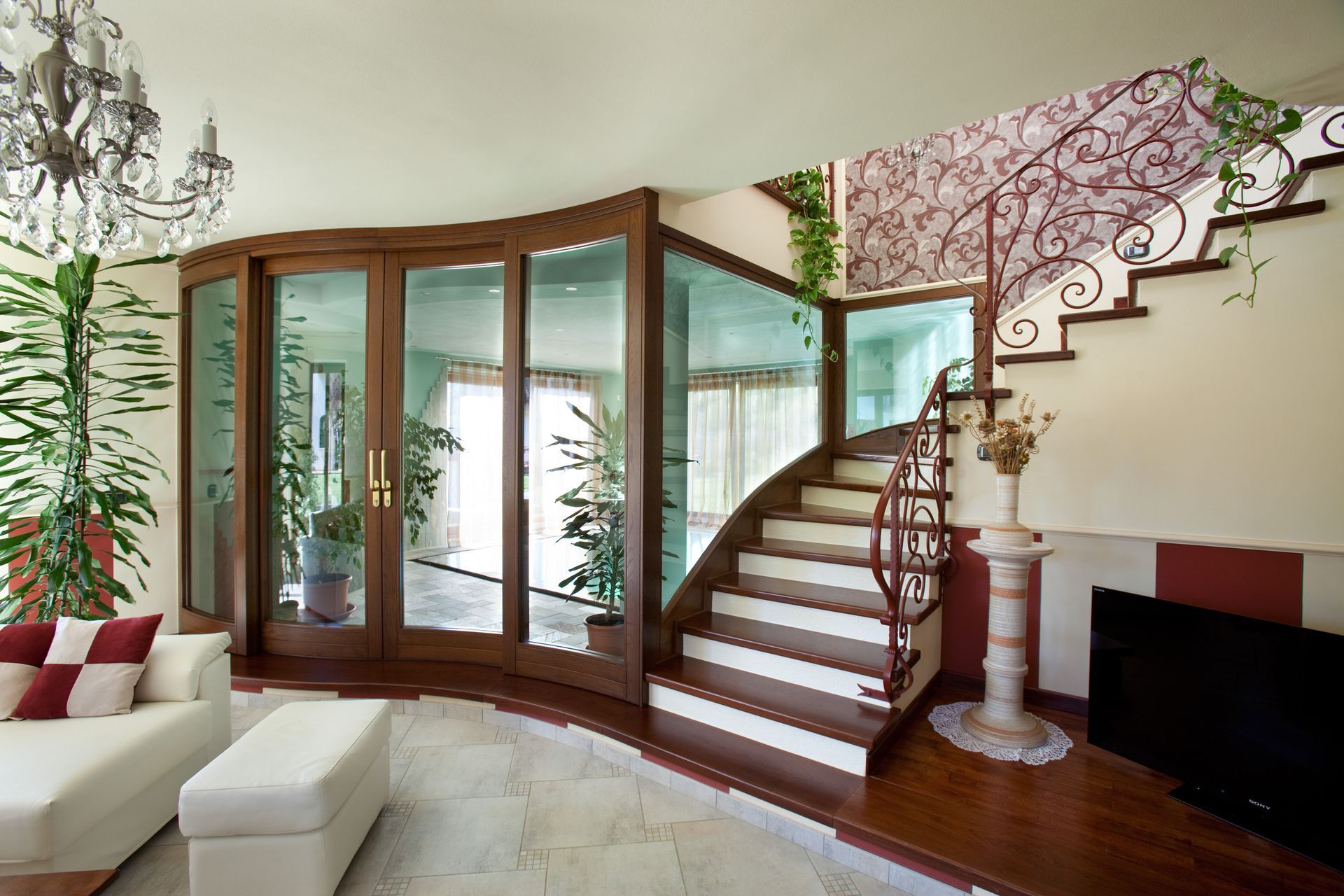 Soggiorno con scala, porte in vetro, finiture in legno, divano bianco e lampadario.