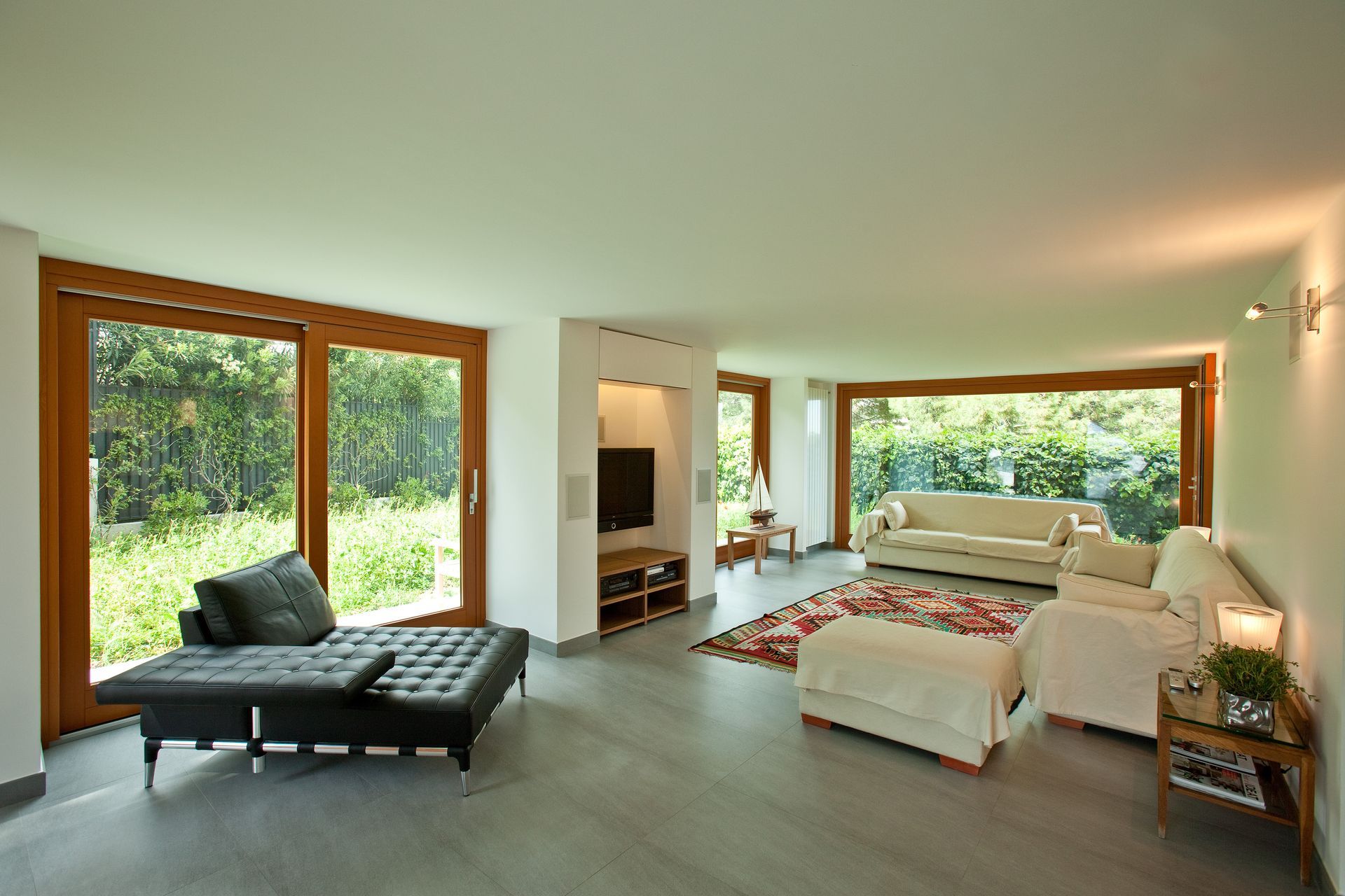Soggiorno con ampie finestre, chaise longue in pelle, divani bianchi e pavimento grigio.