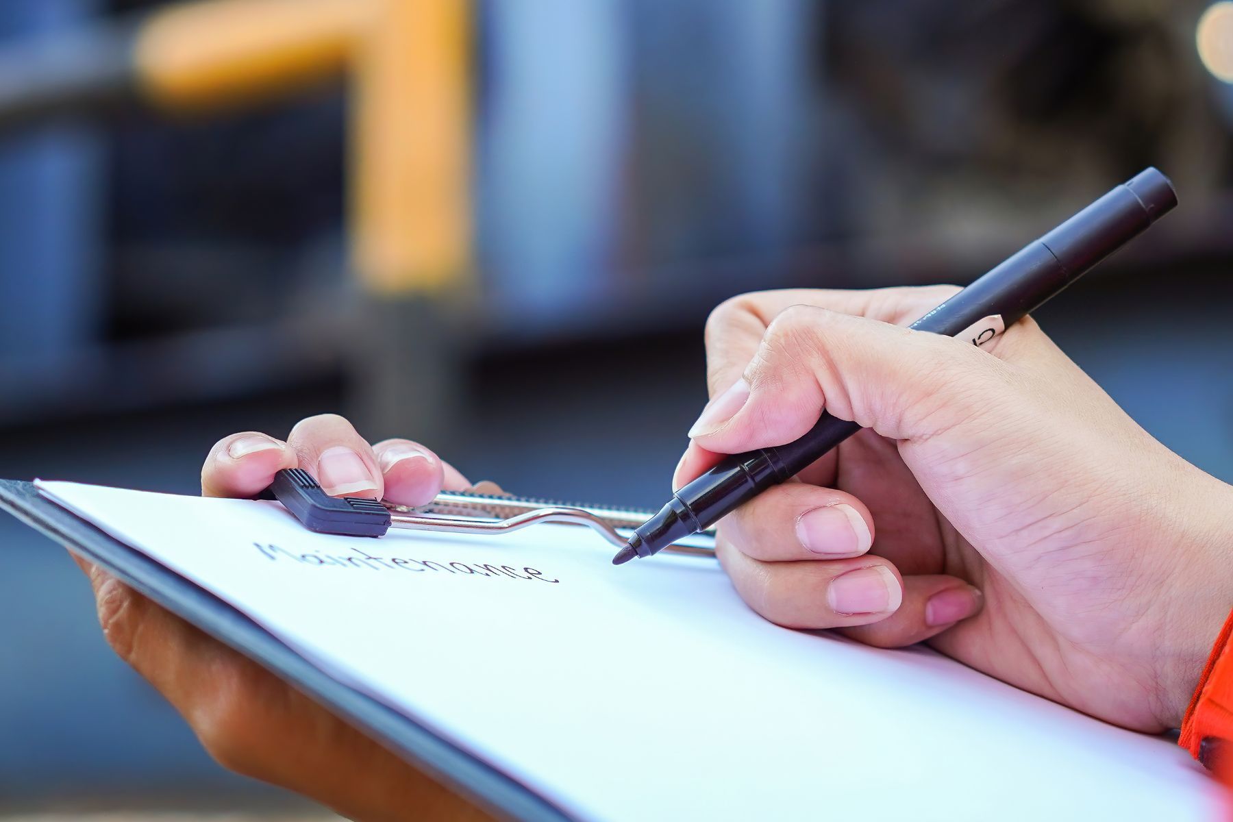 Scrittura a mano su un blocco per appunti con una penna nera, probabilmente mentre prende appunti in un ambiente industriale.