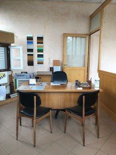 Ufficio con scrivania, sedie, campioni alla parete; porta aperta su un'altra stanza.