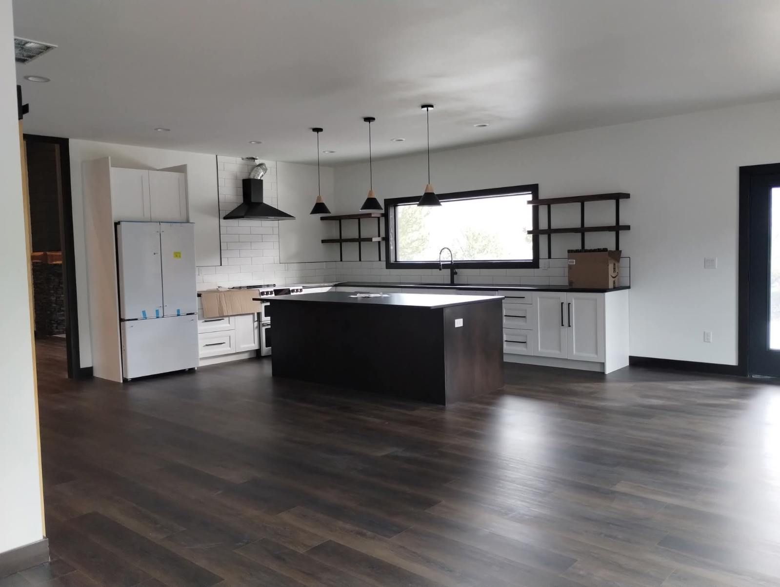 A modern kitchen featuring a dark island, white cabinets, stainless steel appliances, and wood-look flooring.