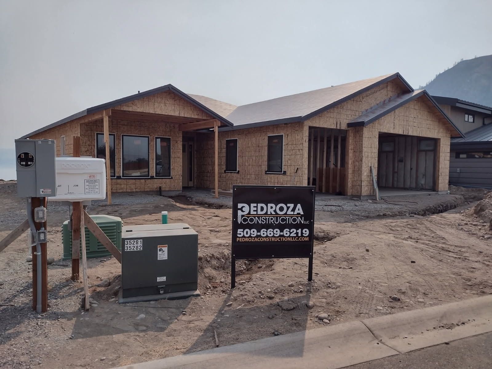 A construction site showing a new house framed with plywood, an electrical box, and a Pedroza Construction sign.