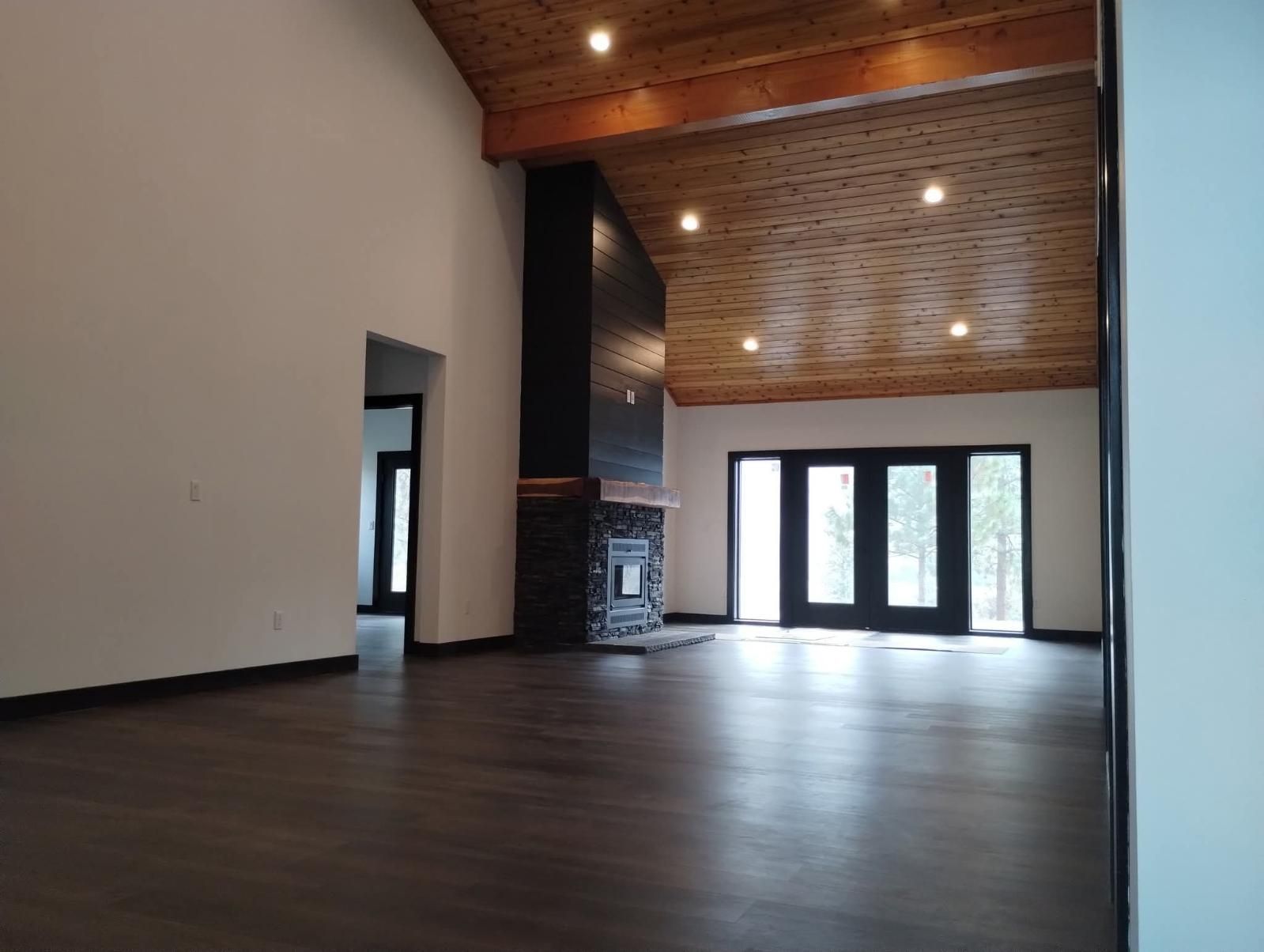 Spacious living area with high, vaulted wood-paneled ceiling, dark stone fireplace, and floor-to-ceiling glass patio doors.