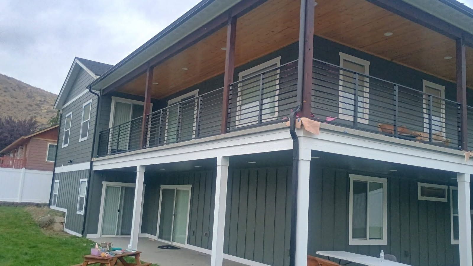 A two-story house with grey vertical siding, a white-railed upper deck, and a lower walk-out patio on a grassy lawn.