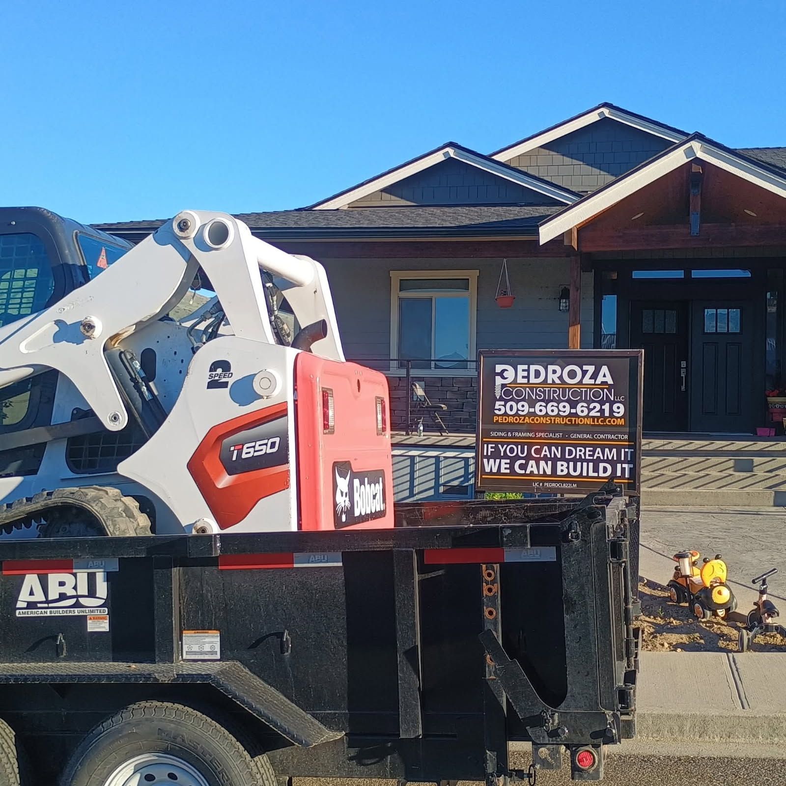 A white and red Bobcat skid steer on a black trailer parked in front of a house, with a Pedroza Construction sign nearby.
