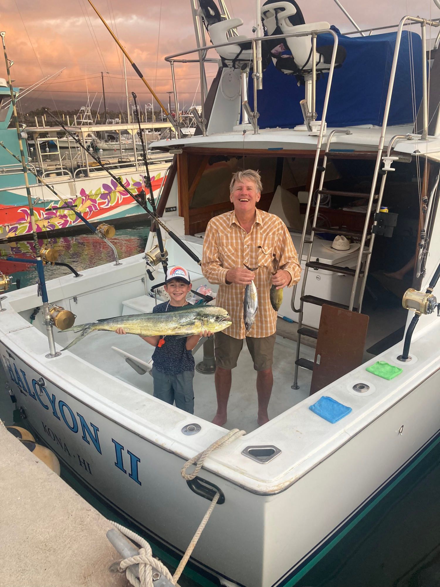 A man and a boy are standing on the deck of a boat holding a fish.