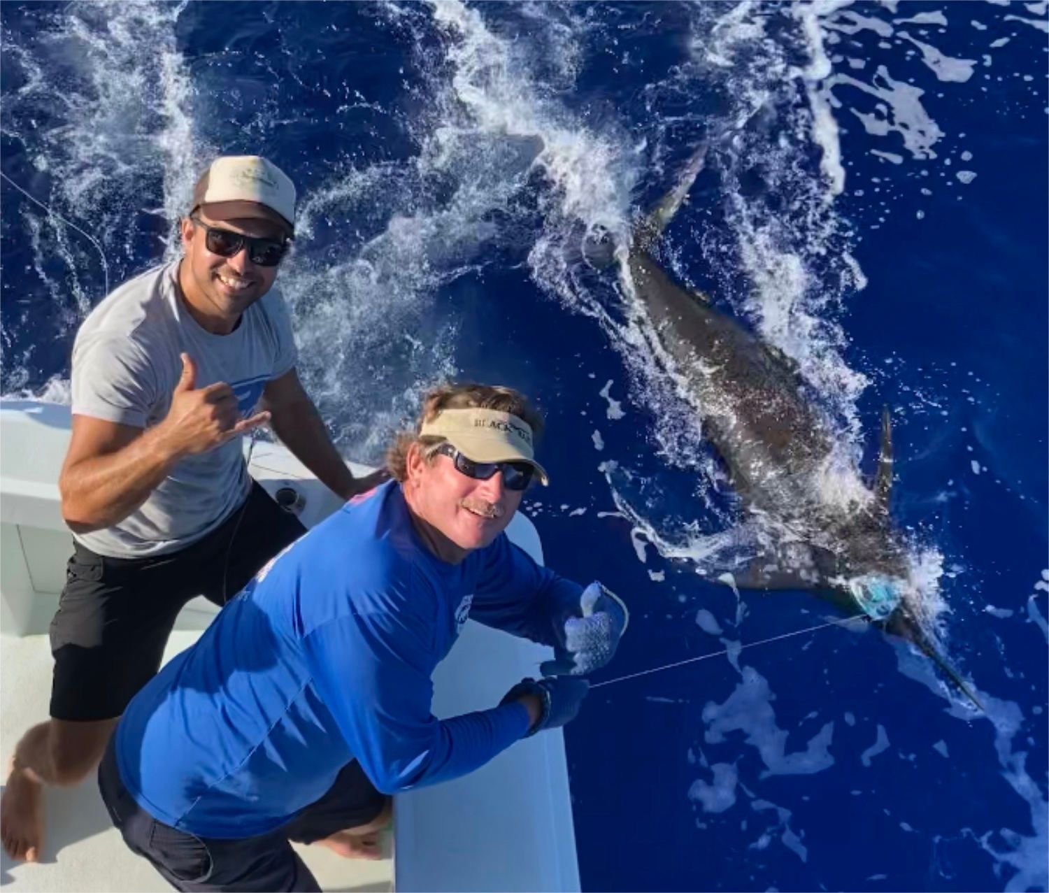 Two men on a boat with a dolphin in the background