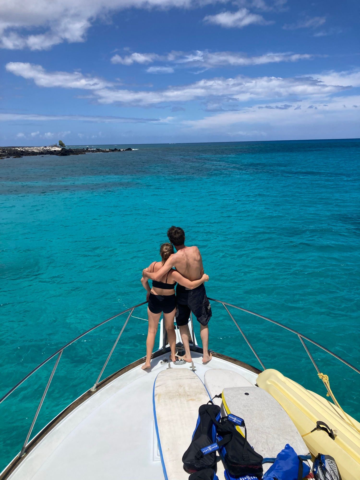 A man and a woman are hugging on the back of a boat in the ocean.