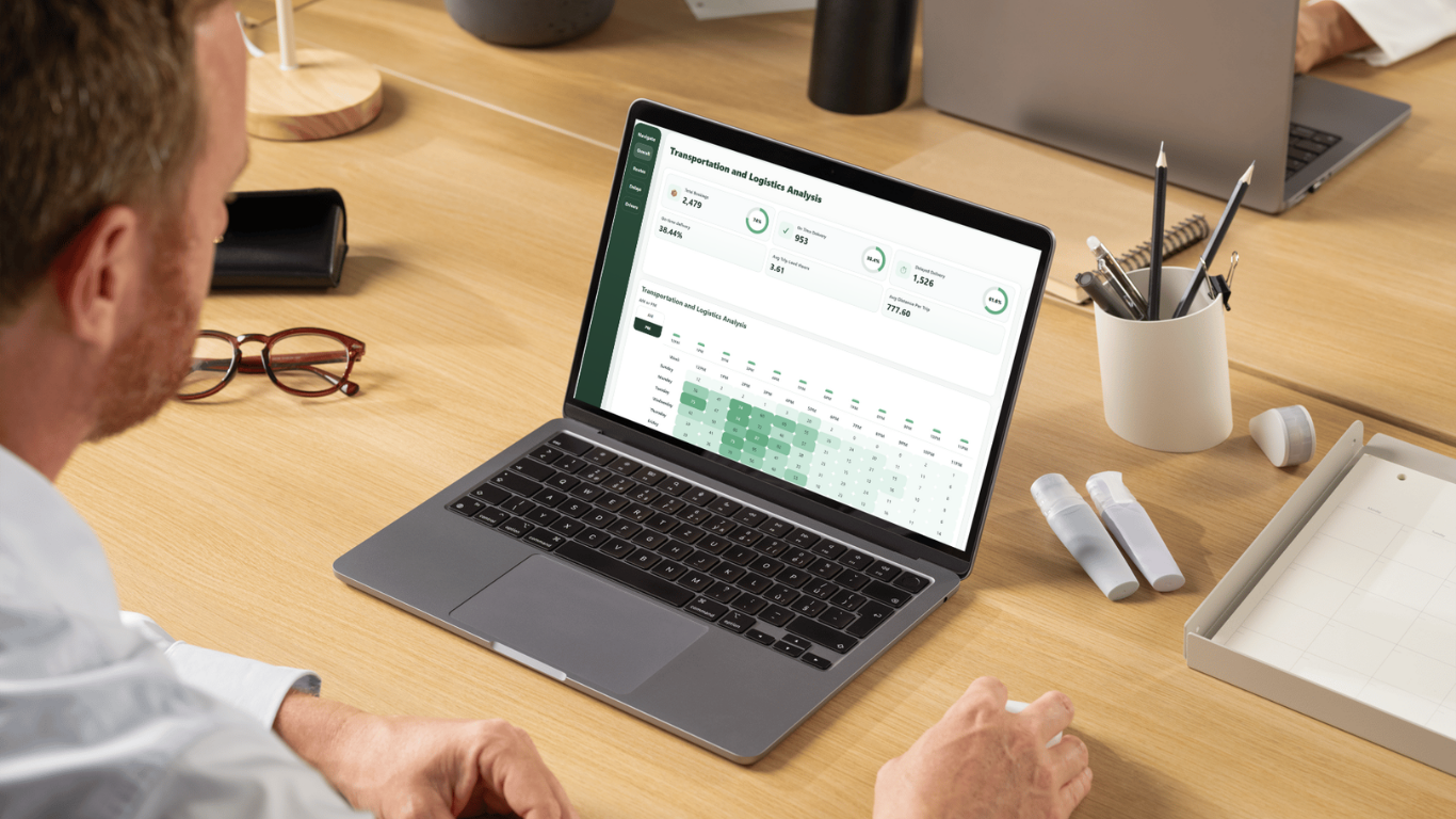 Een persoon werkt op een laptop aan een houten bureau met koffie, een bril en kantoorbenodigdheden.