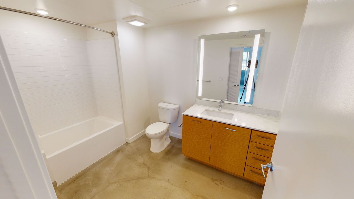 Bathroom with white walls, tub/shower, toilet, wooden vanity, and large mirror.