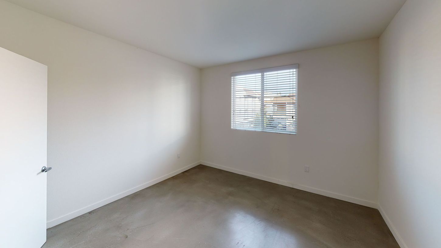 Empty room with white walls, a window covered with plastic, and a gray floor.