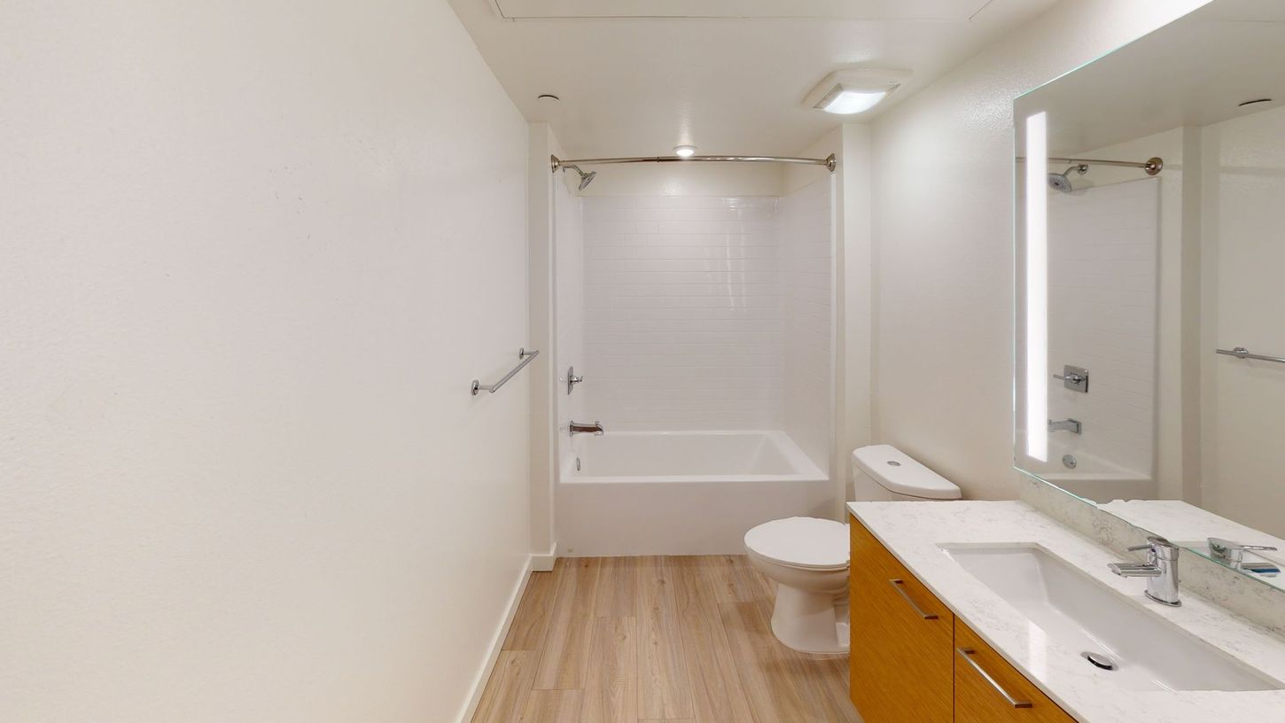 Bathroom with white walls, light wood floor, toilet, tub/shower, and vanity with a mirror.