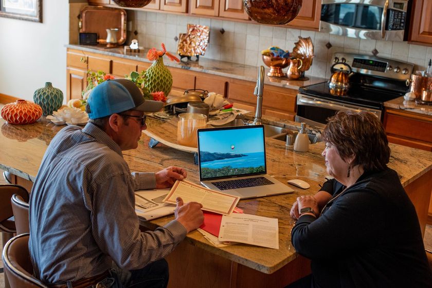 Two people reviewing paperwork at a kitchen table with a laptop open