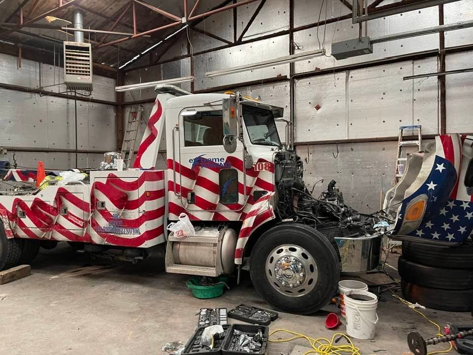 Damaged truck wrapped in American flag graphics inside a garage, with debris and tools on the floor