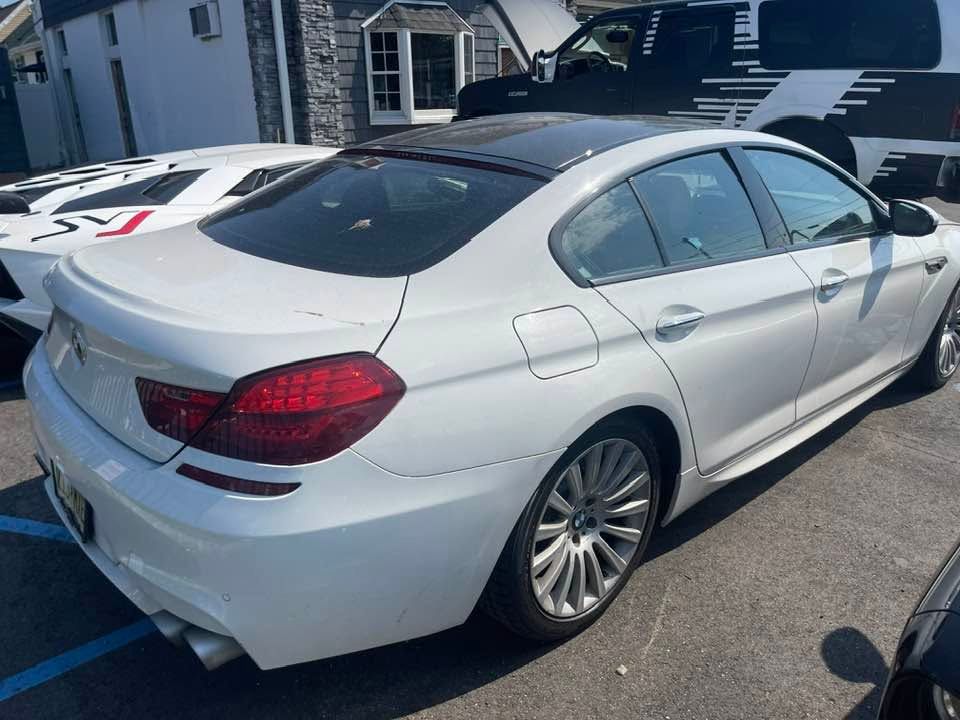 White sedan parked in a lot, rear side view, with black roof and tinted windows.