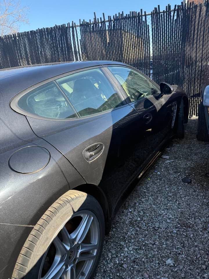 Black sports car parked beside a wooden fence on a gravel lot.