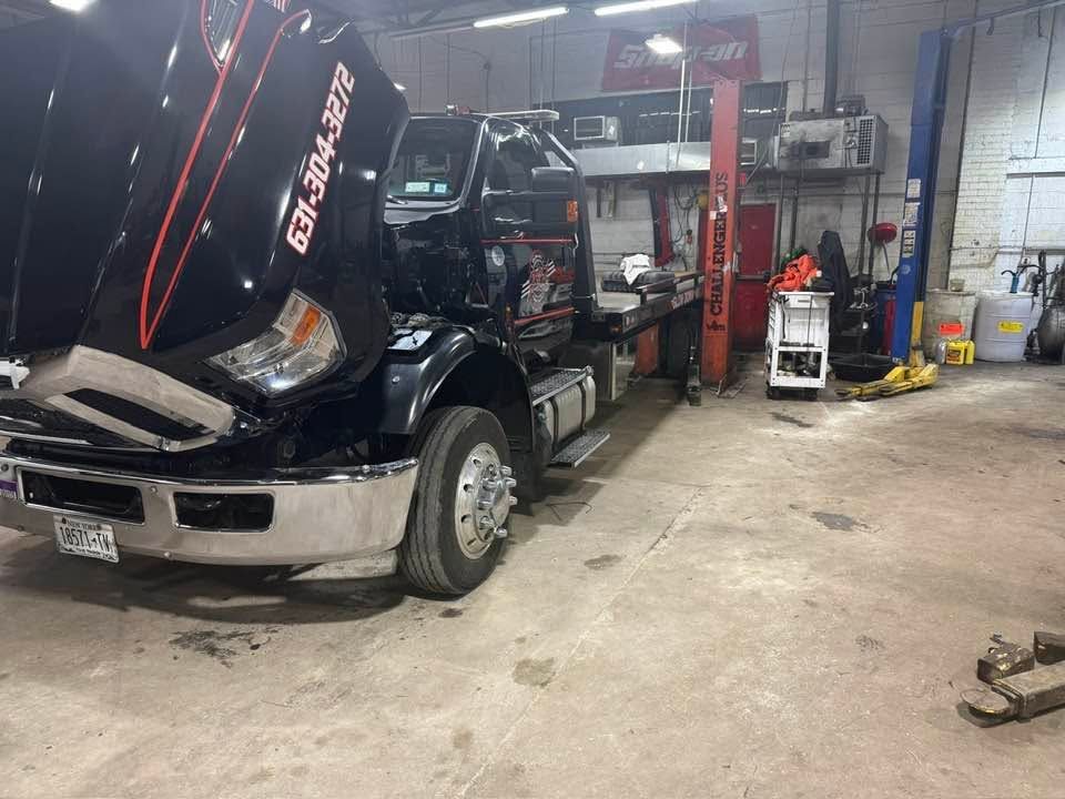Black semi-truck with hood raised in an auto repair shop garage.