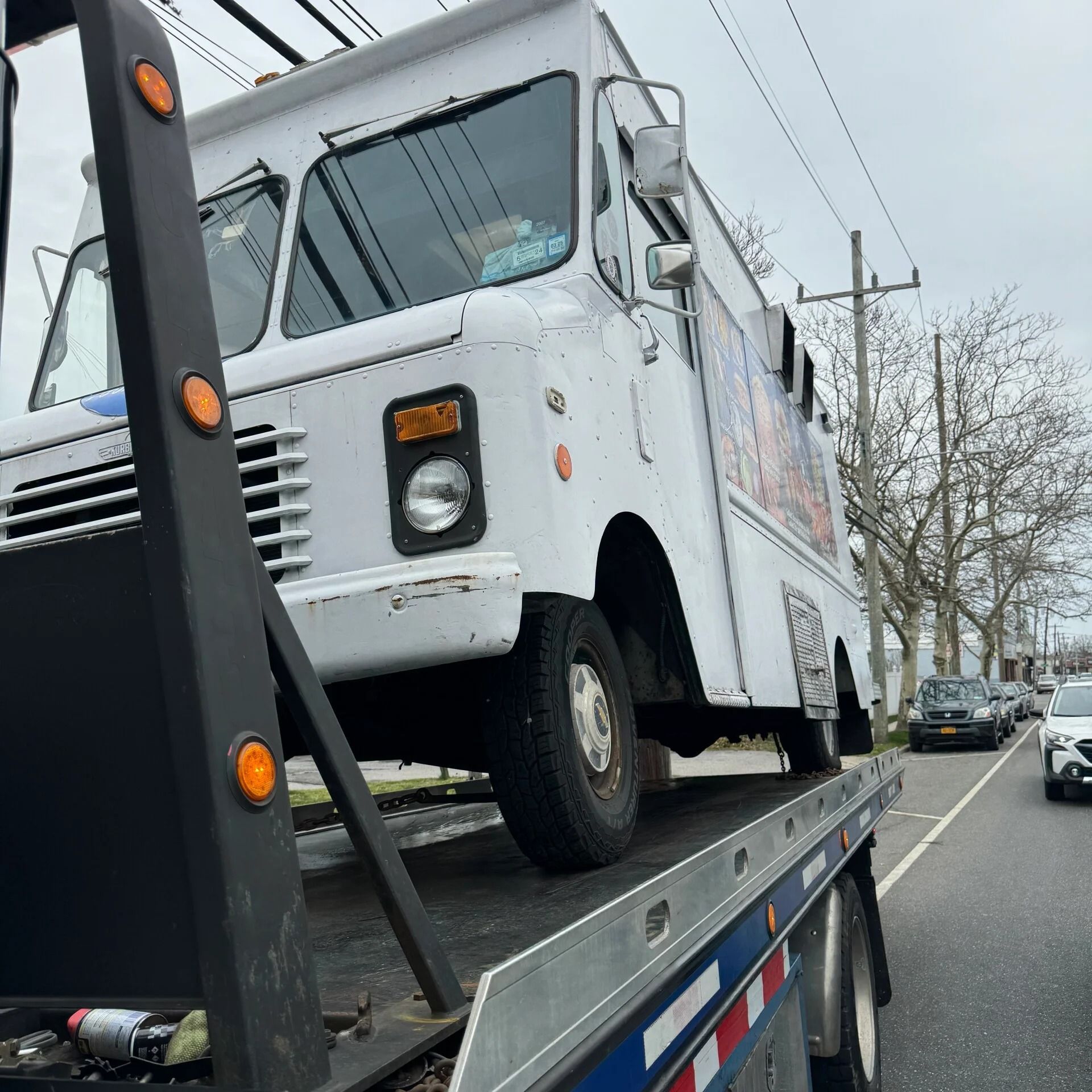 White step van on a flatbed tow truck parked along a city street.