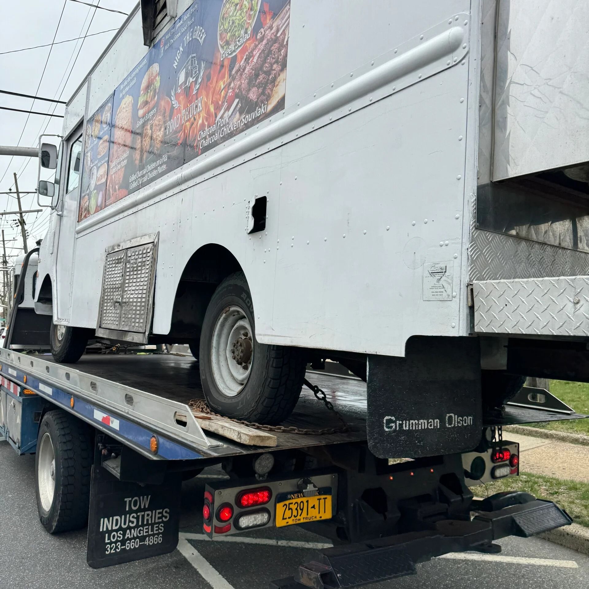 White utility truck on a tow flatbed, rear wheel visible, with a city street background.