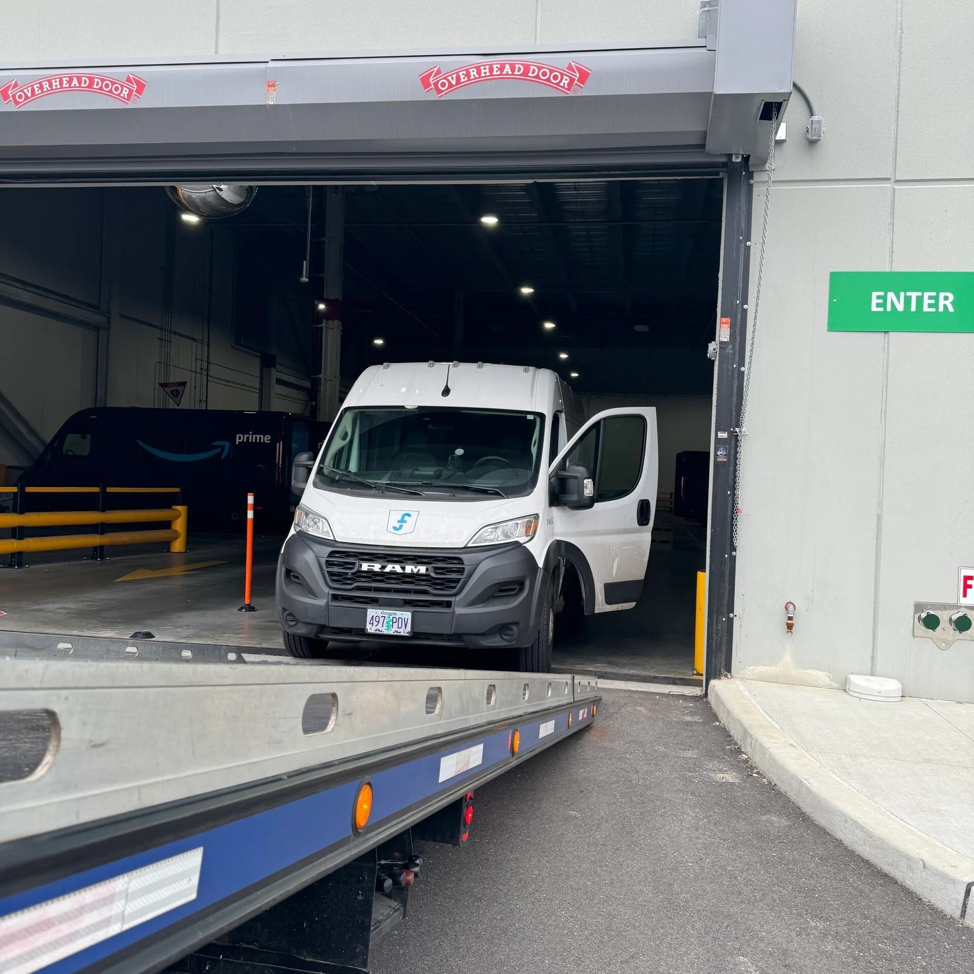 White delivery van at warehouse entrance with open side door and loading ramp in front