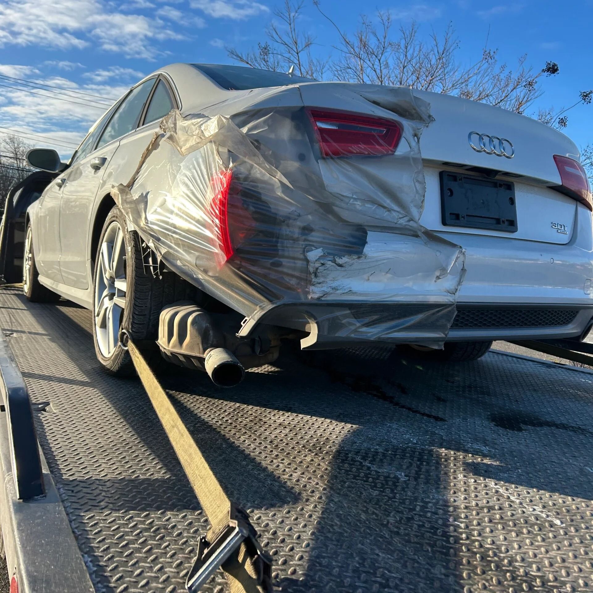Damaged silver Audi sedan strapped on a tow truck flatbed after rear-end collision