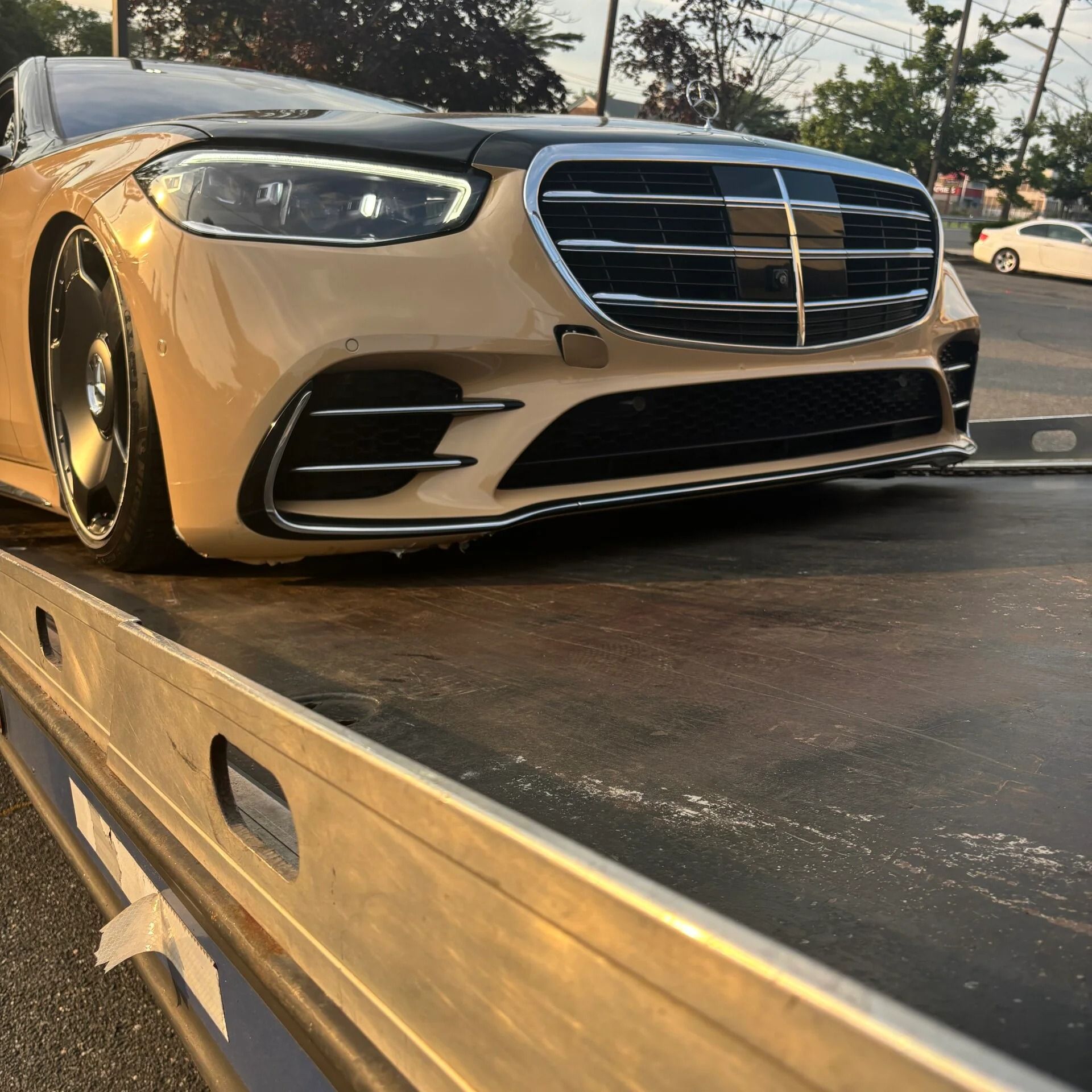 Beige Mercedes sedan on a flatbed tow truck at sunset, front view from low angle