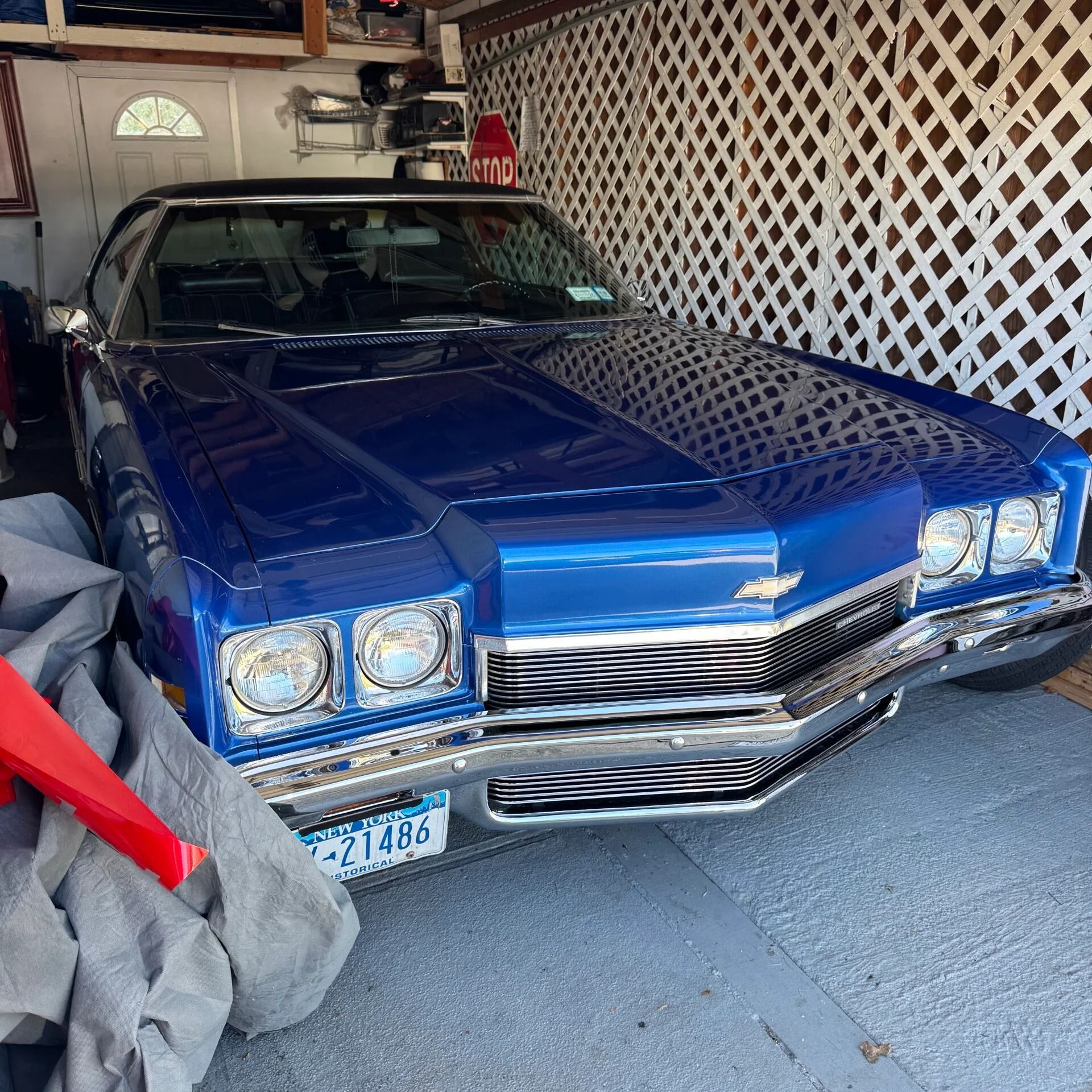 Blue classic car parked in a garage, with chrome front grille and lattice wall backdrop