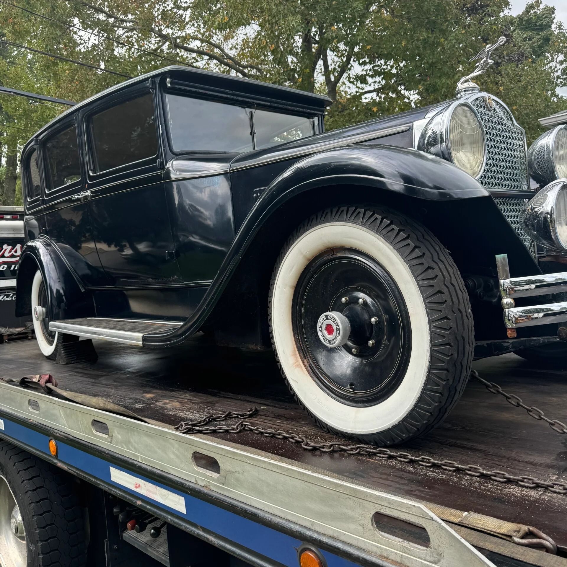 Black vintage classic car with whitewall tires on a flatbed trailer outdoors
