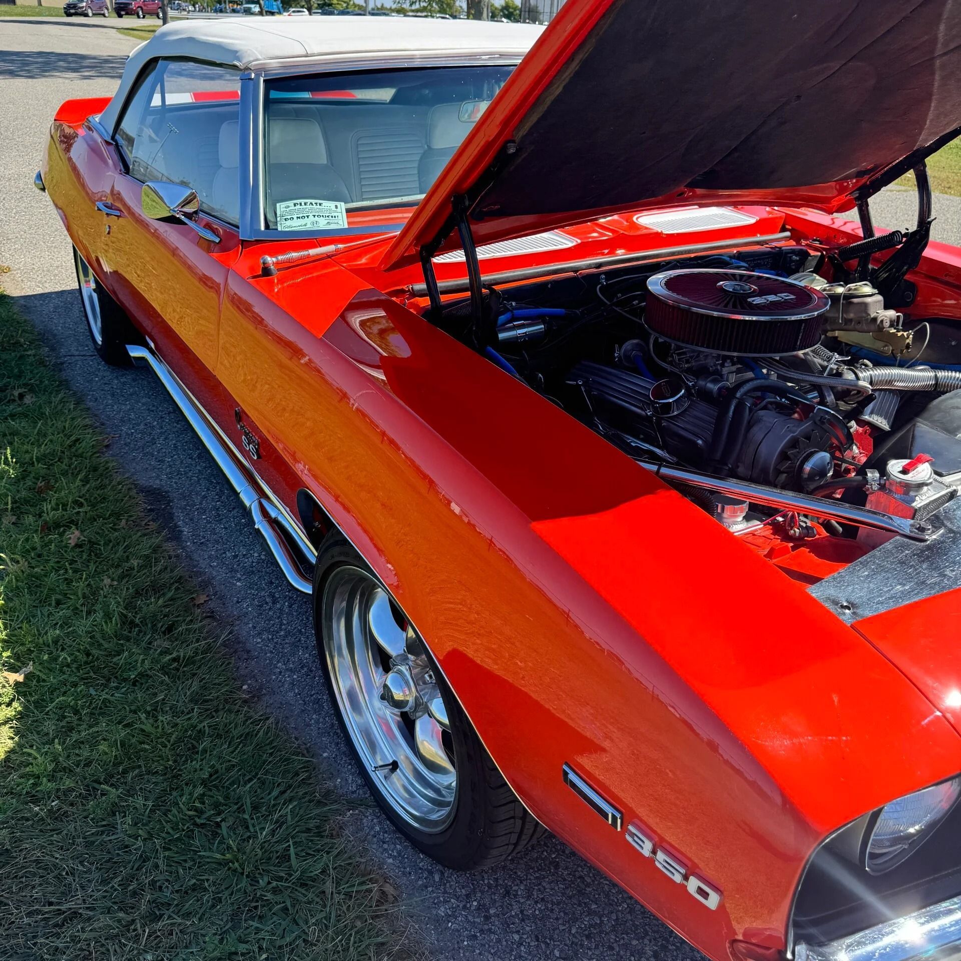 Red classic muscle car with hood open, showing engine at an outdoor car show.