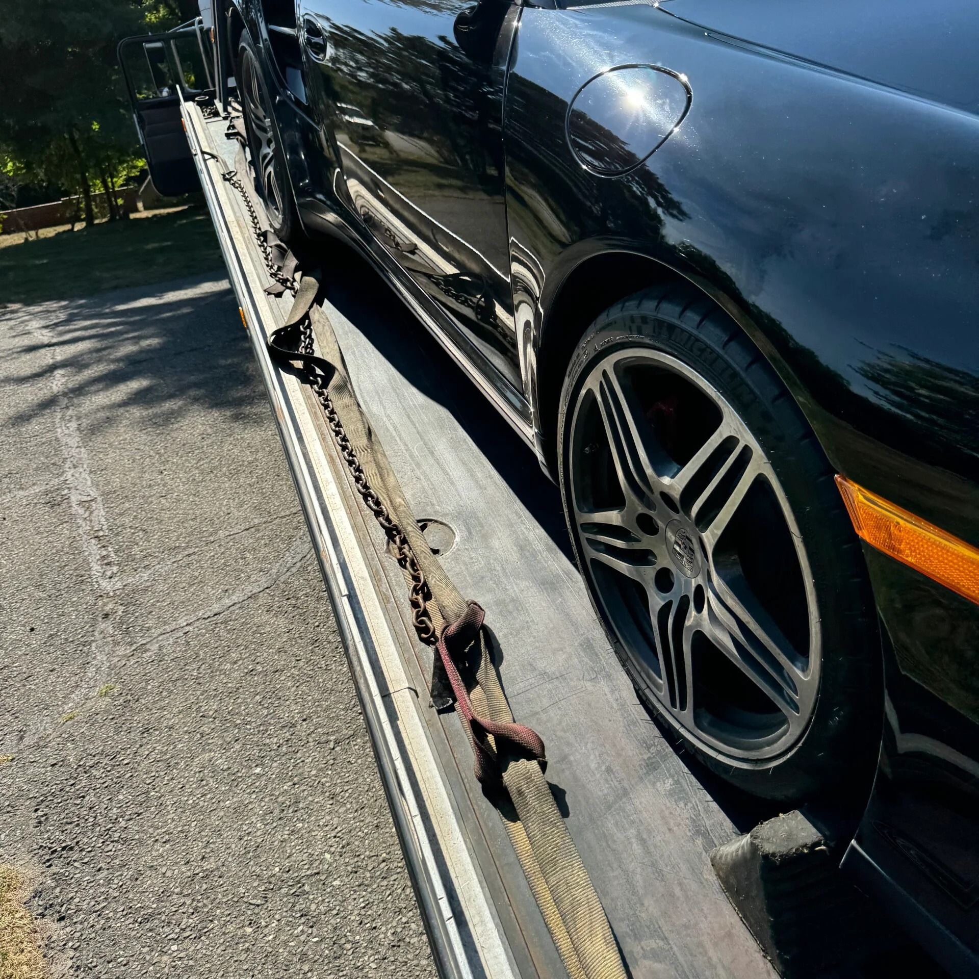 Black sports car strapped to a tow truck flatbed on a sunny street