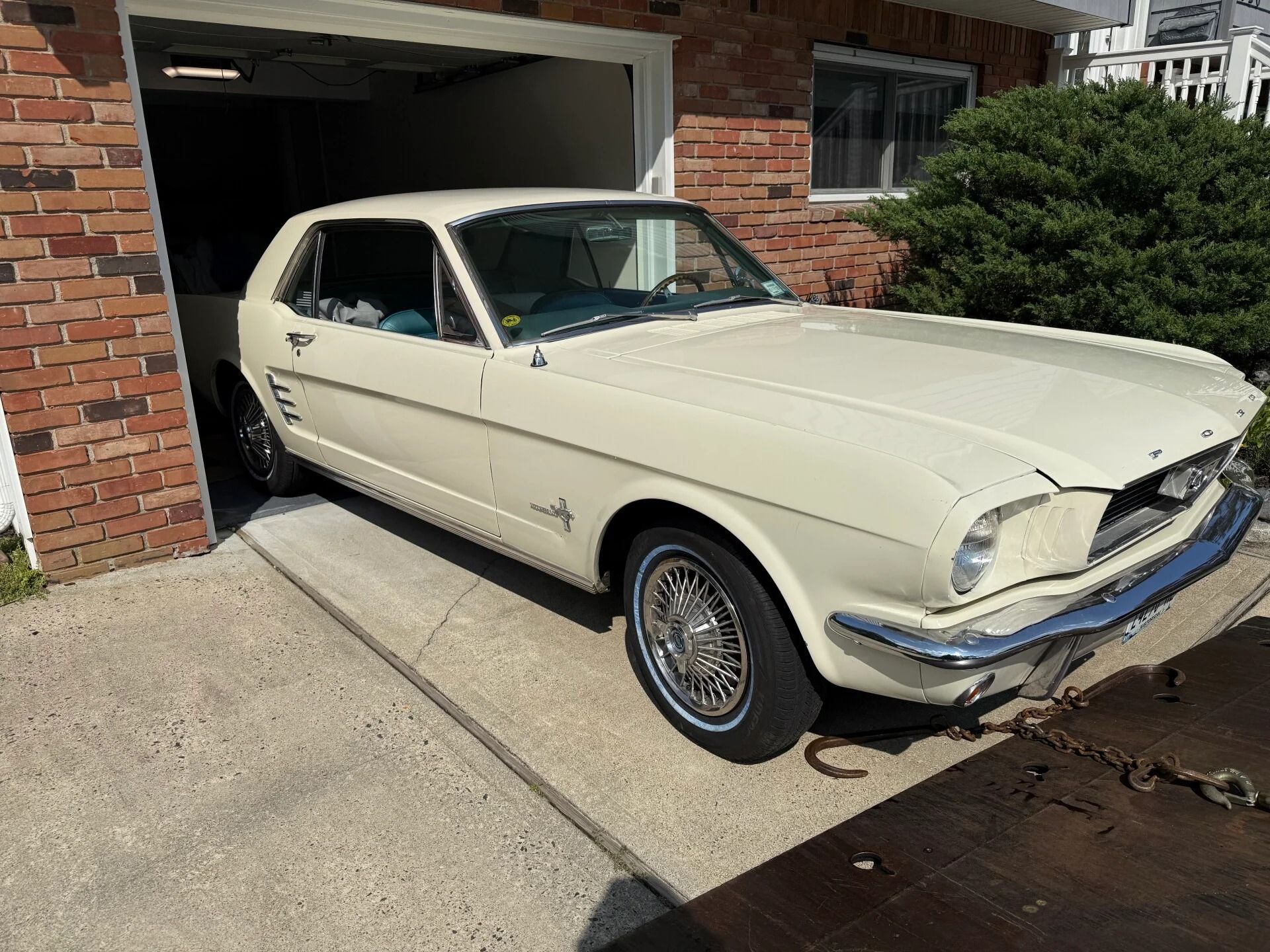 Cream-colored classic coupe parked halfway out of a brick garage driveway