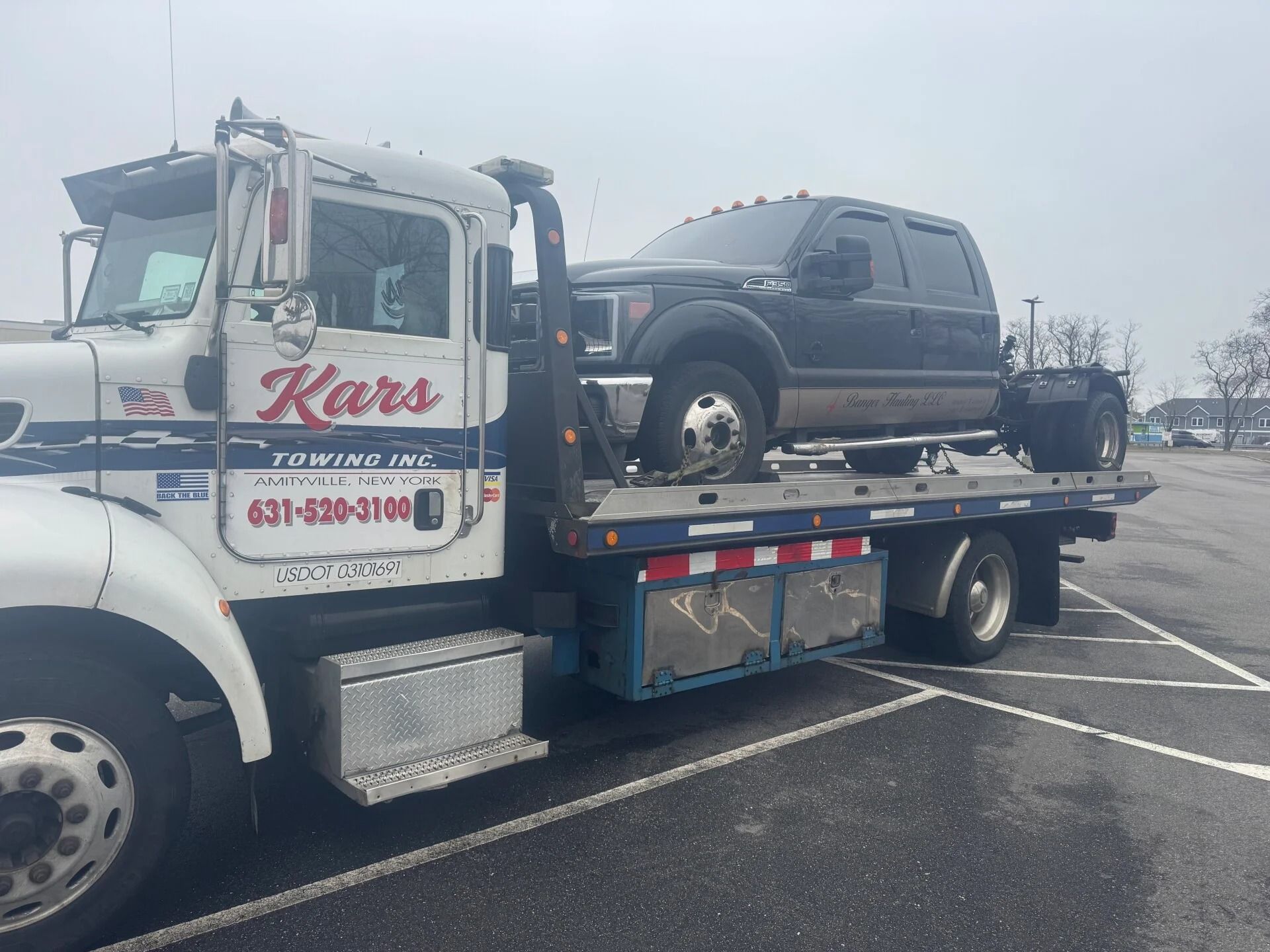 Tow truck hauling a black pickup in a parking lot on a cloudy day