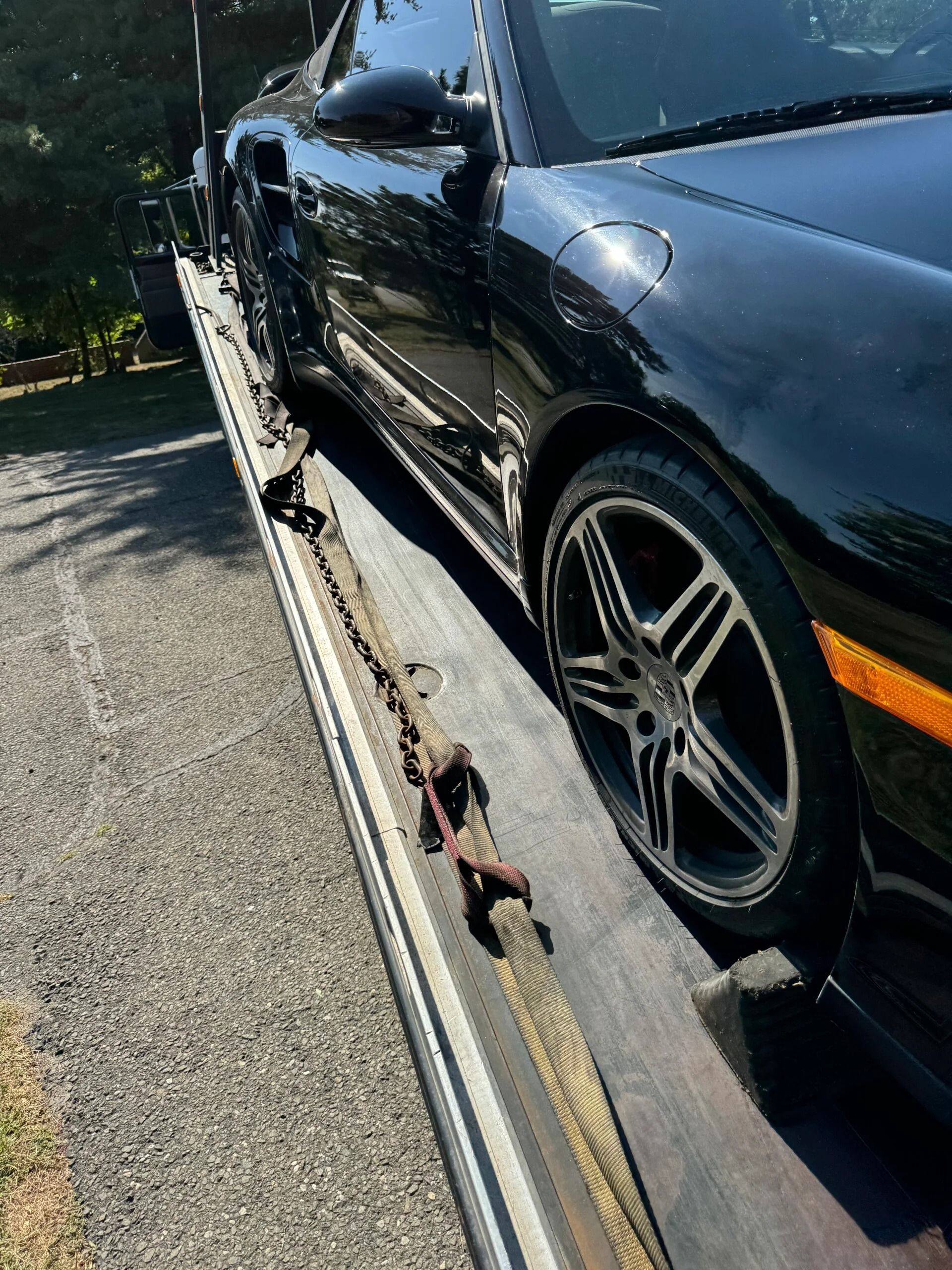 Black sports car damaged on a flatbed tow truck, with a front wheel visible.