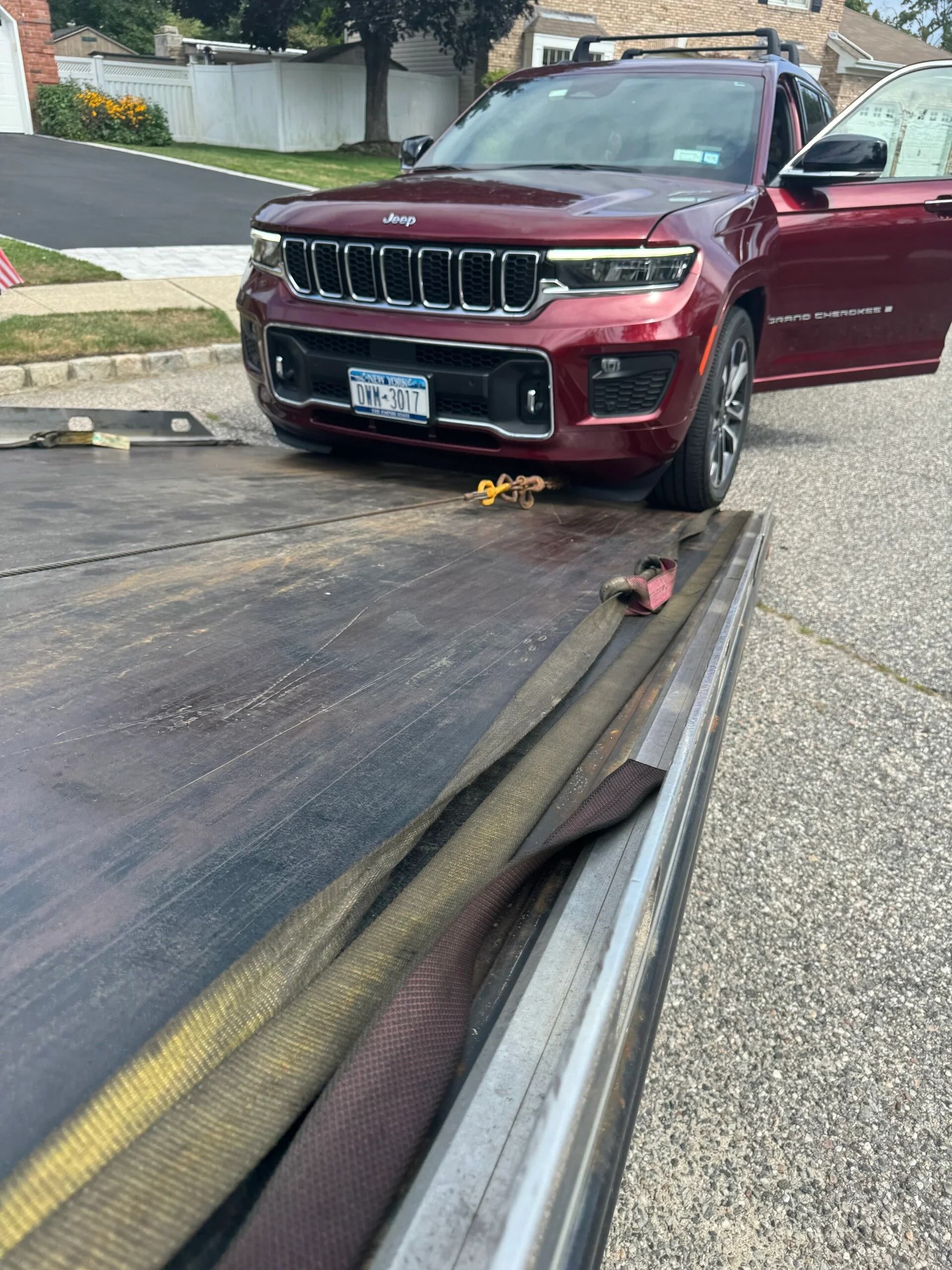 Red SUV on a burnt roadway with smoke damage; driver’s door open near a curb.