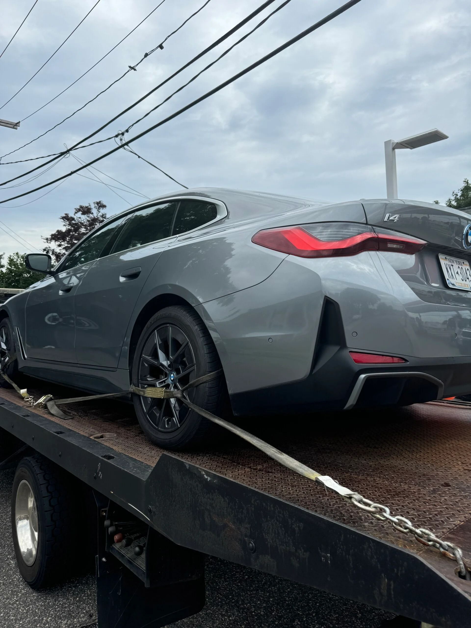 Gray sports car strapped on a tow truck flatbed outdoors under cloudy sky