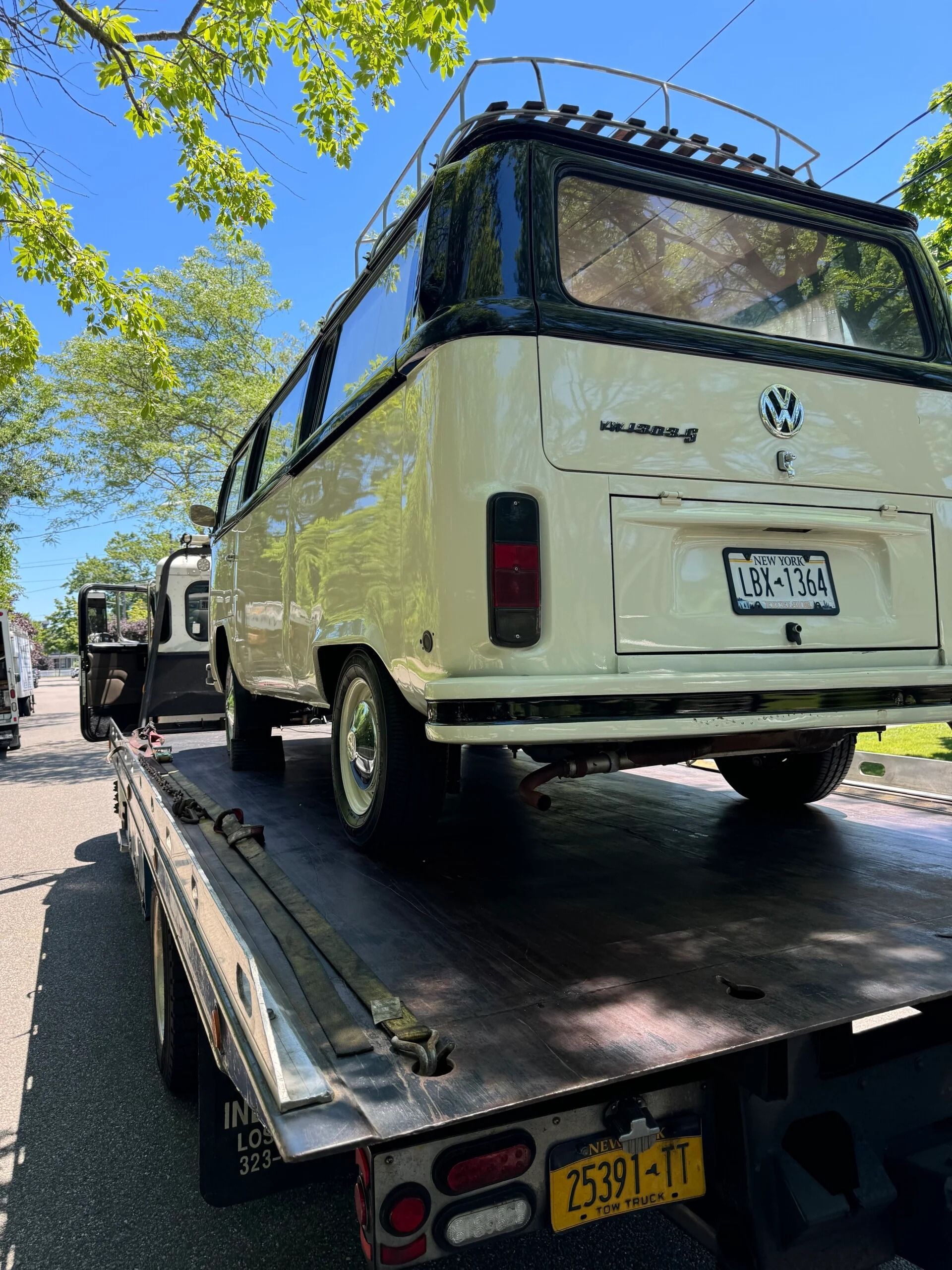 White vintage van on a flatbed tow truck outdoors under trees, rear view.