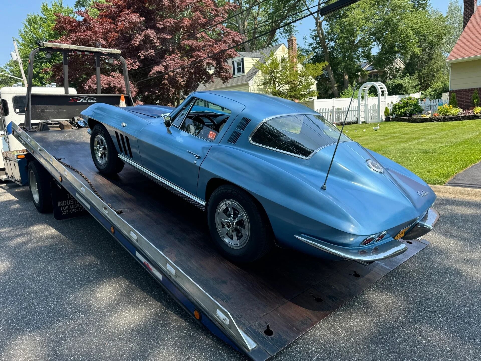 Blue classic sports car secured on a flatbed trailer in a suburban driveway