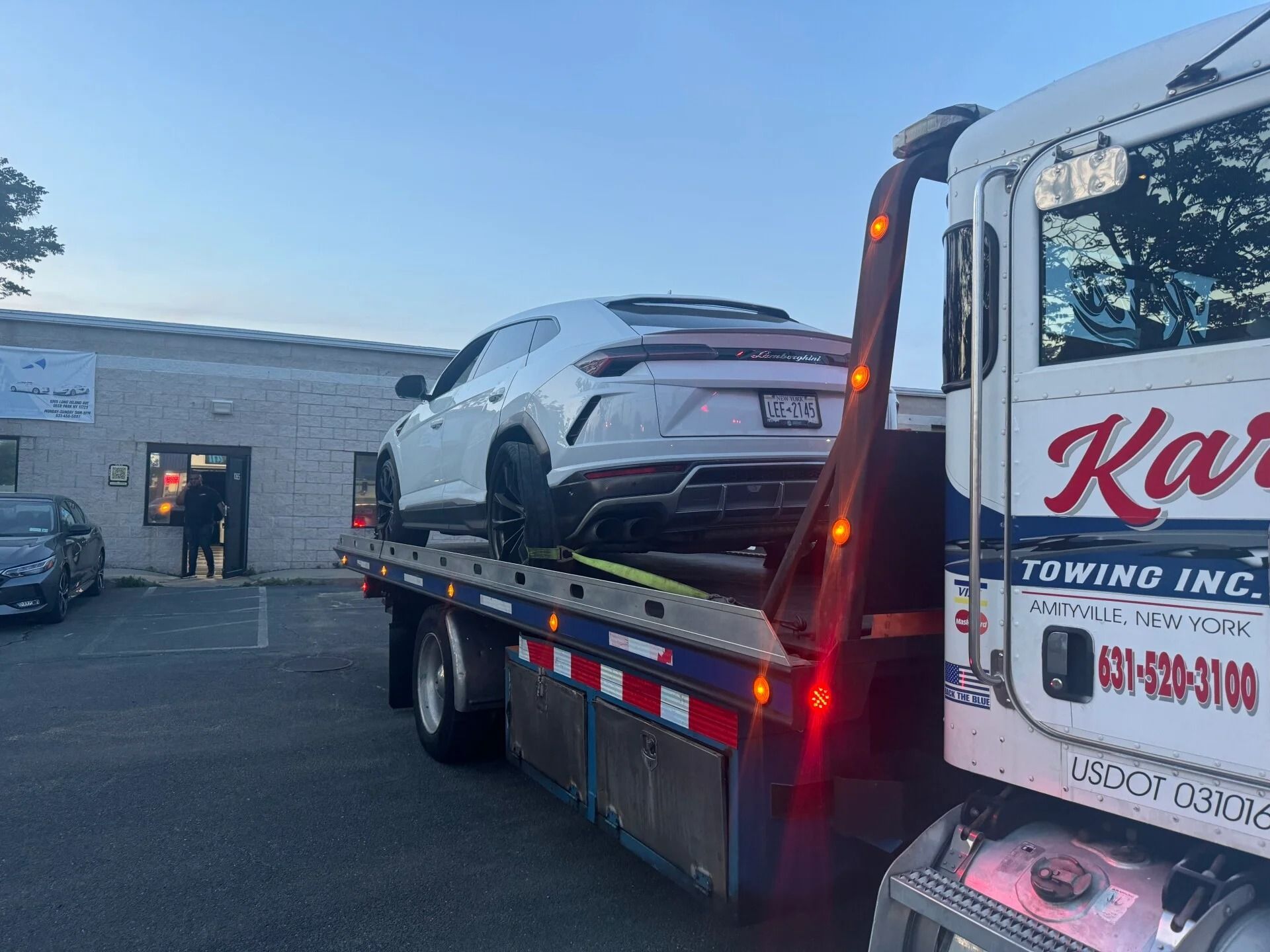 Car carrier tow truck with a white sports car parked outside a garage at dusk