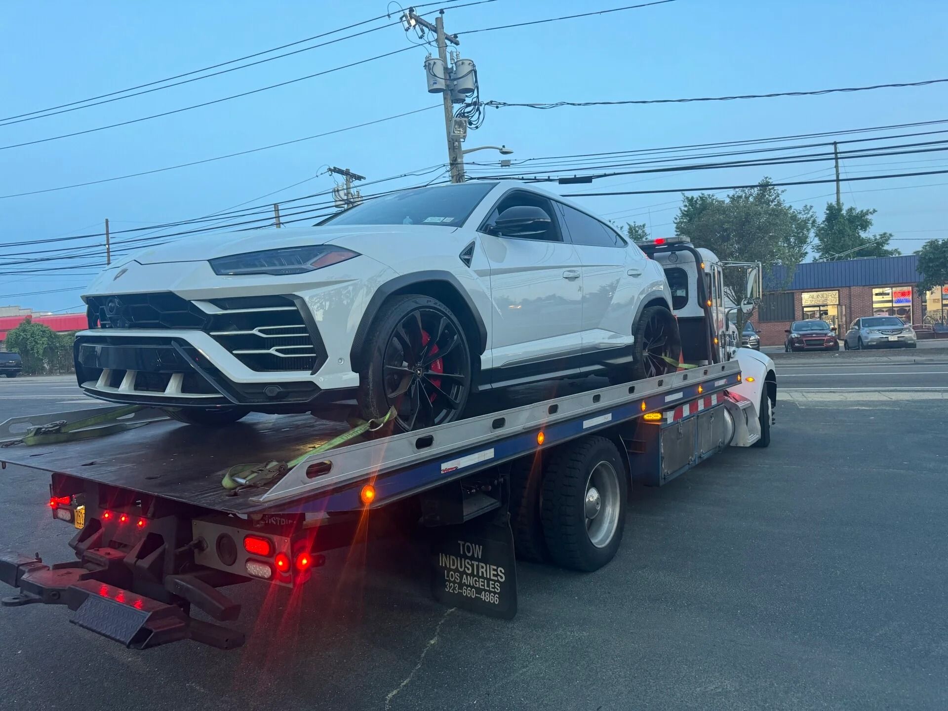 White sports car on a flatbed tow truck at dusk on a roadside.