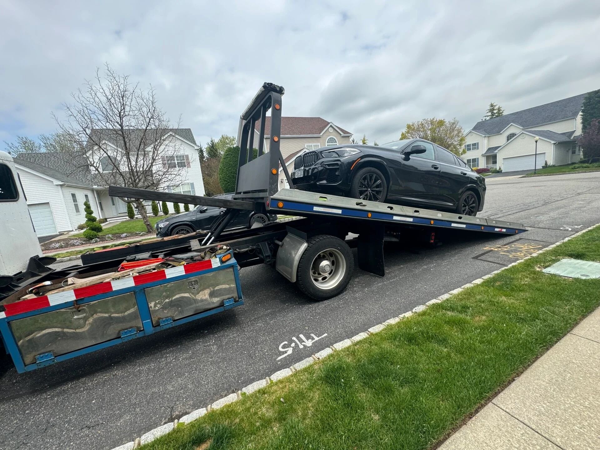 Tow truck loading a black sports car on a blue flatbed trailer along a suburban street