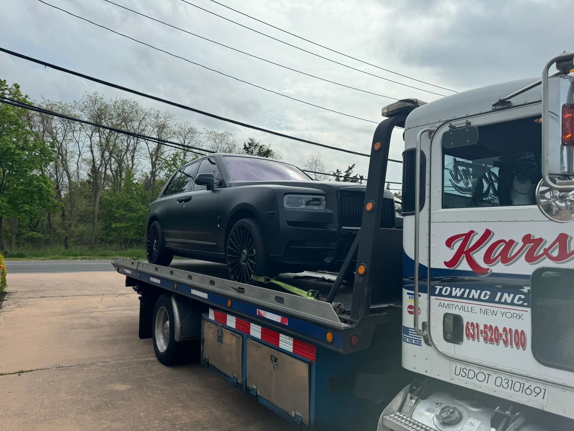 Black SUV on a tow truck beside a road under cloudy skies