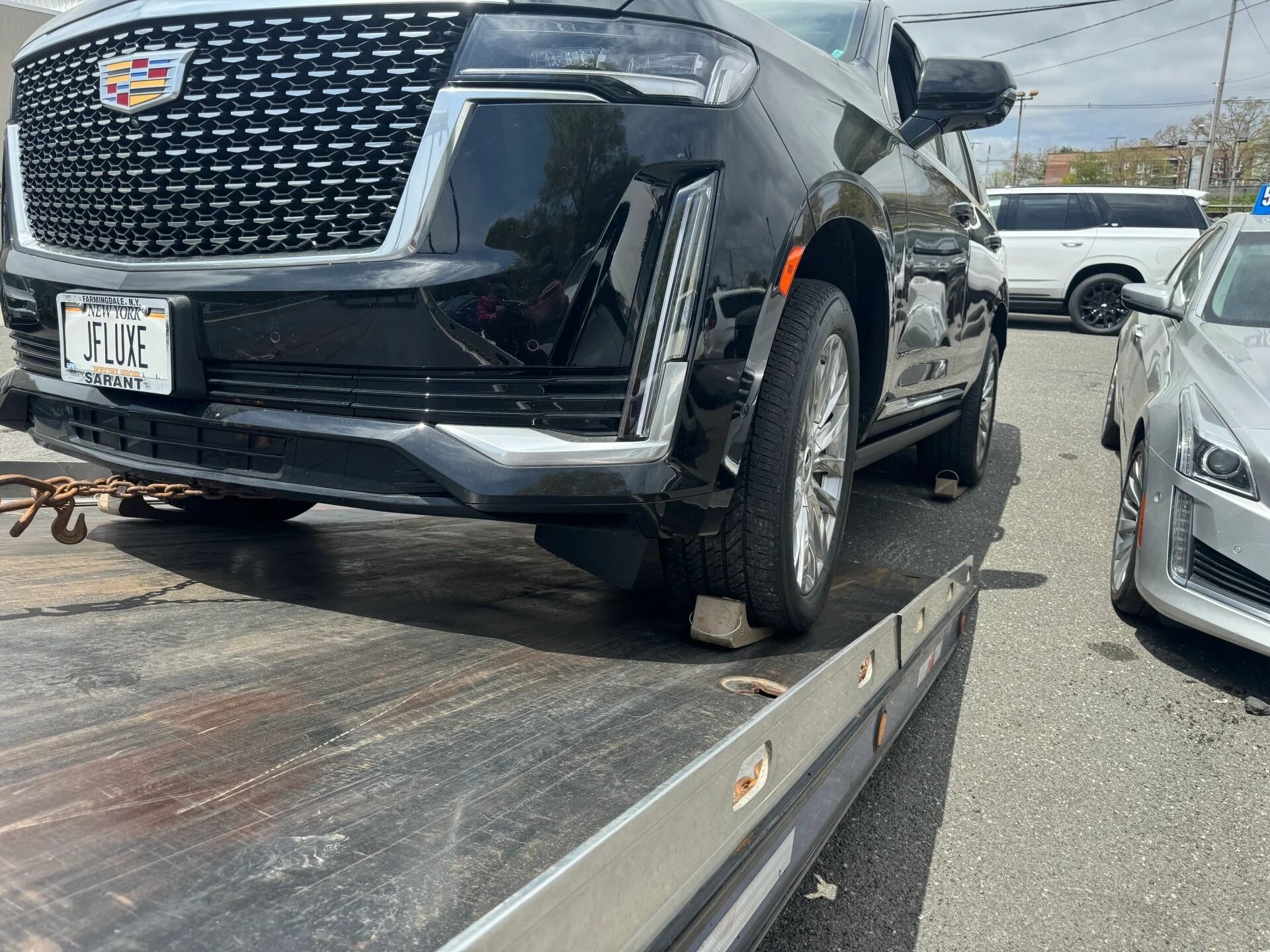 Black SUV on a tow truck flatbed in a parking lot, with a silver car beside it.
