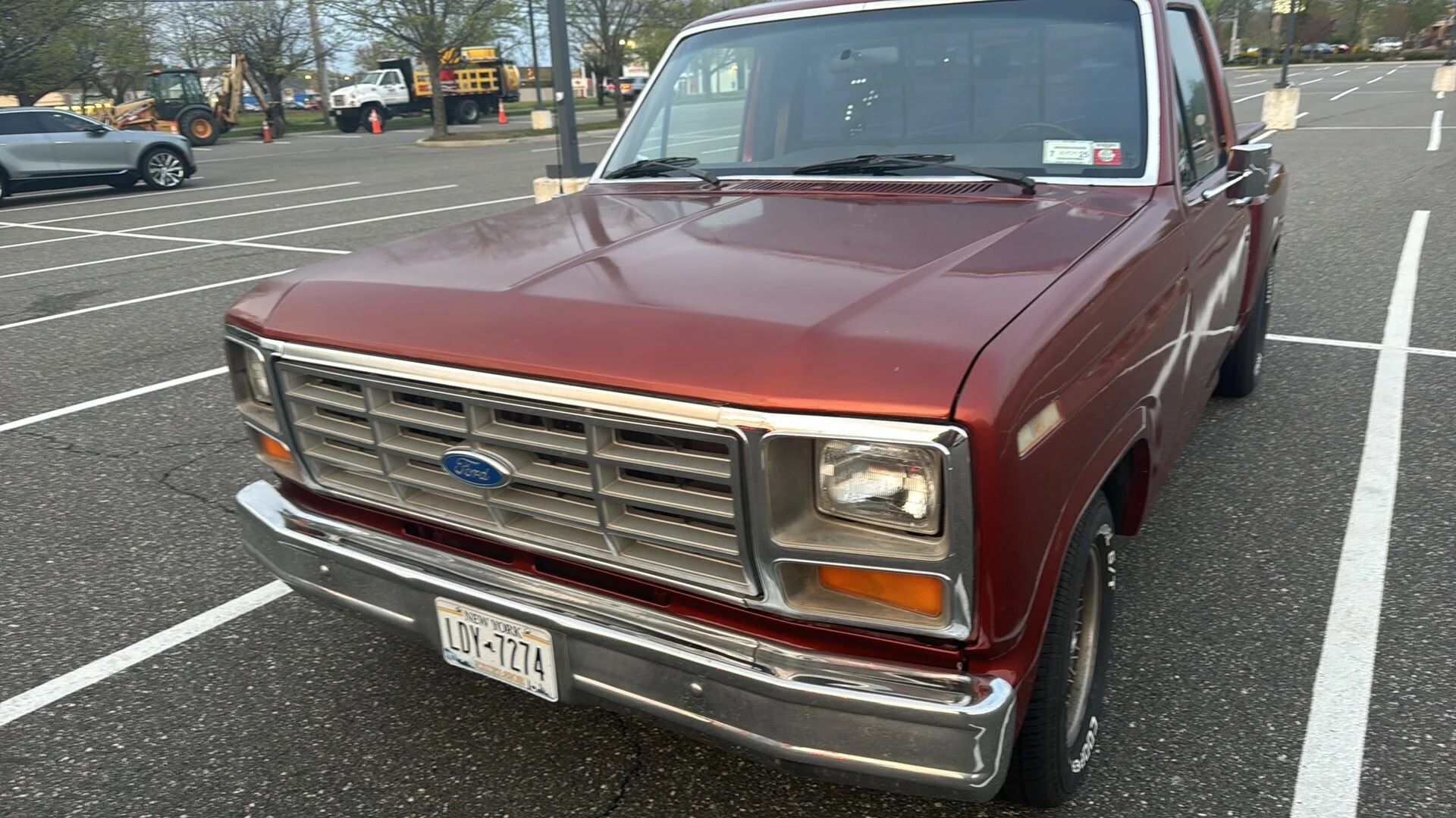 Maroon pickup truck parked in a marked parking lot, front view with chrome grille.