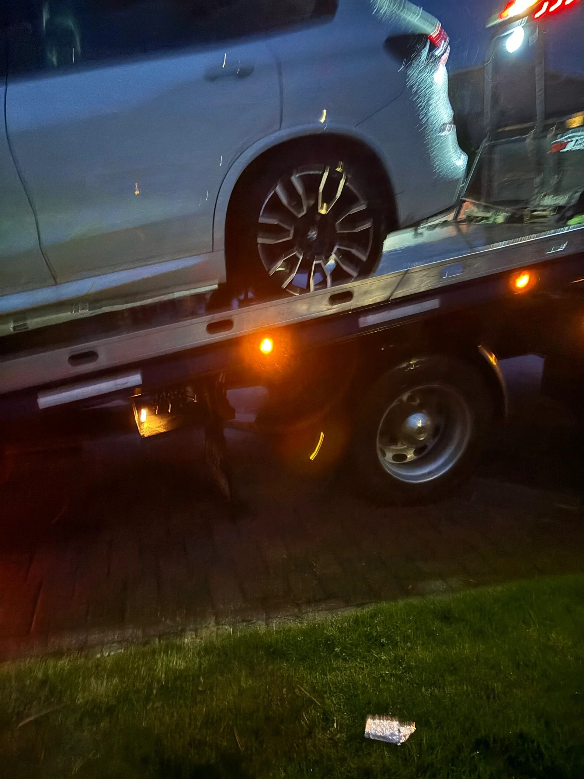 Car on a tow truck at night, with an amber light glowing beneath the flatbed.