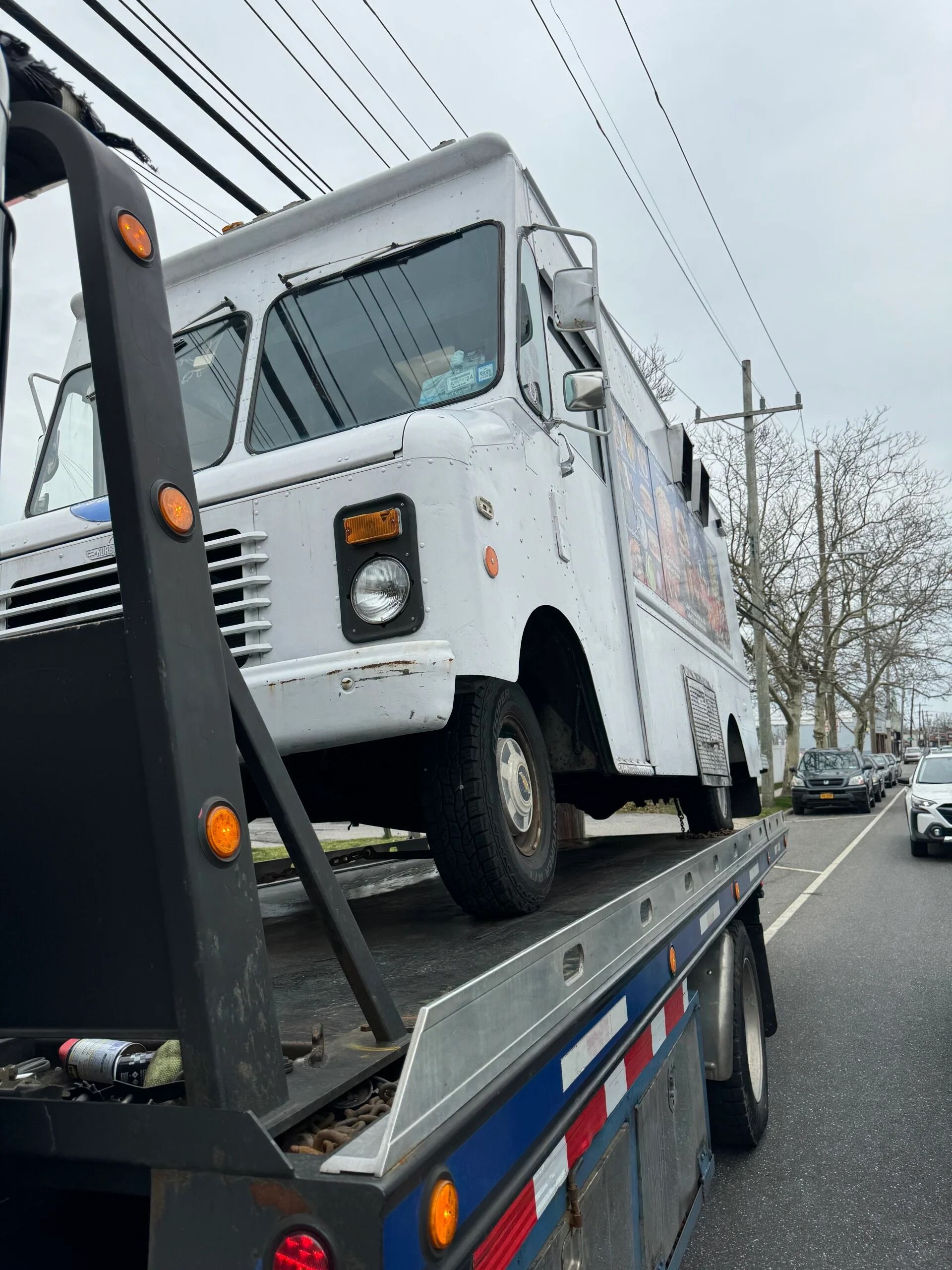 White utility truck loaded on a blue flatbed tow truck on a roadside, viewed from the rear angle
