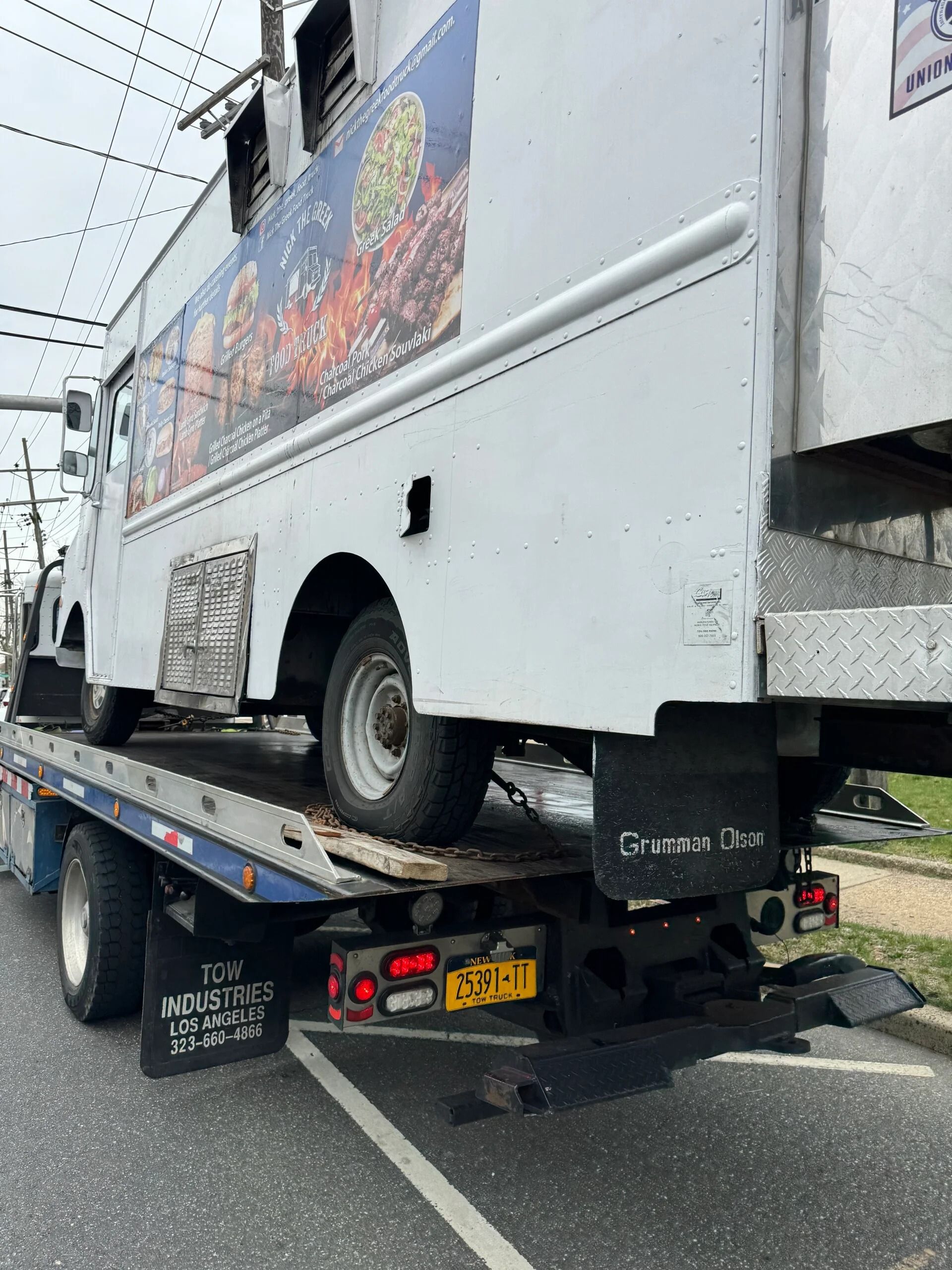 White truck on tow truck bed after collision, rear wheel visible on road