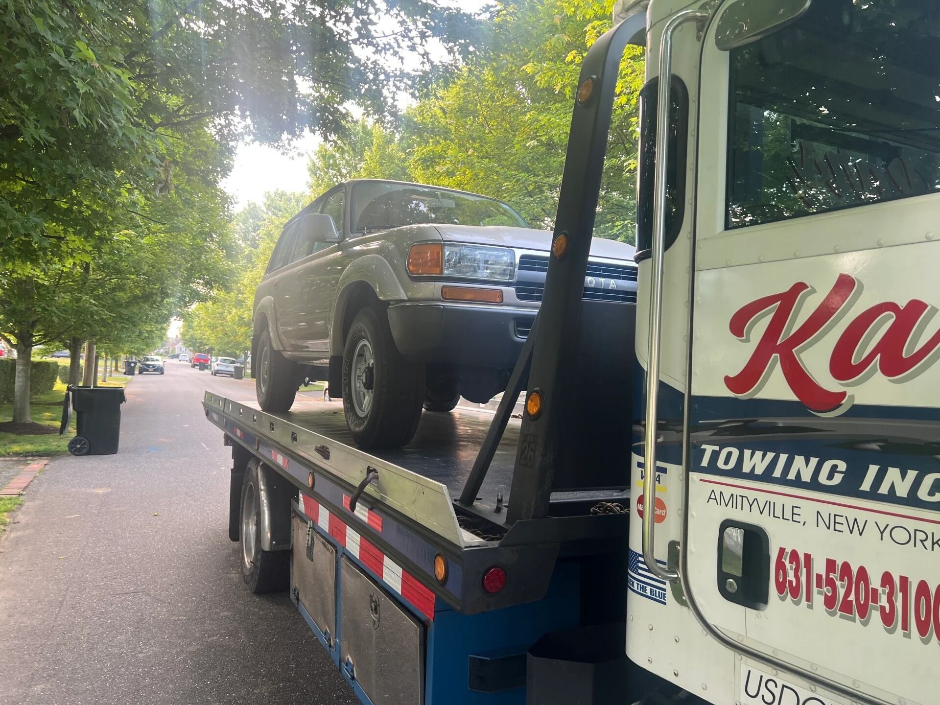 Tow truck hauling a silver SUV on a tree-lined residential street