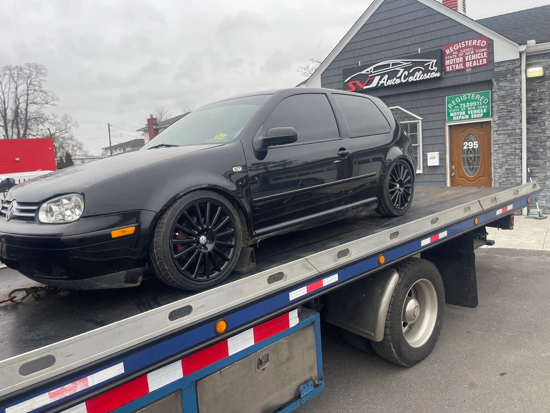 Black sedan on a flatbed tow truck outside a building with Arabic signage